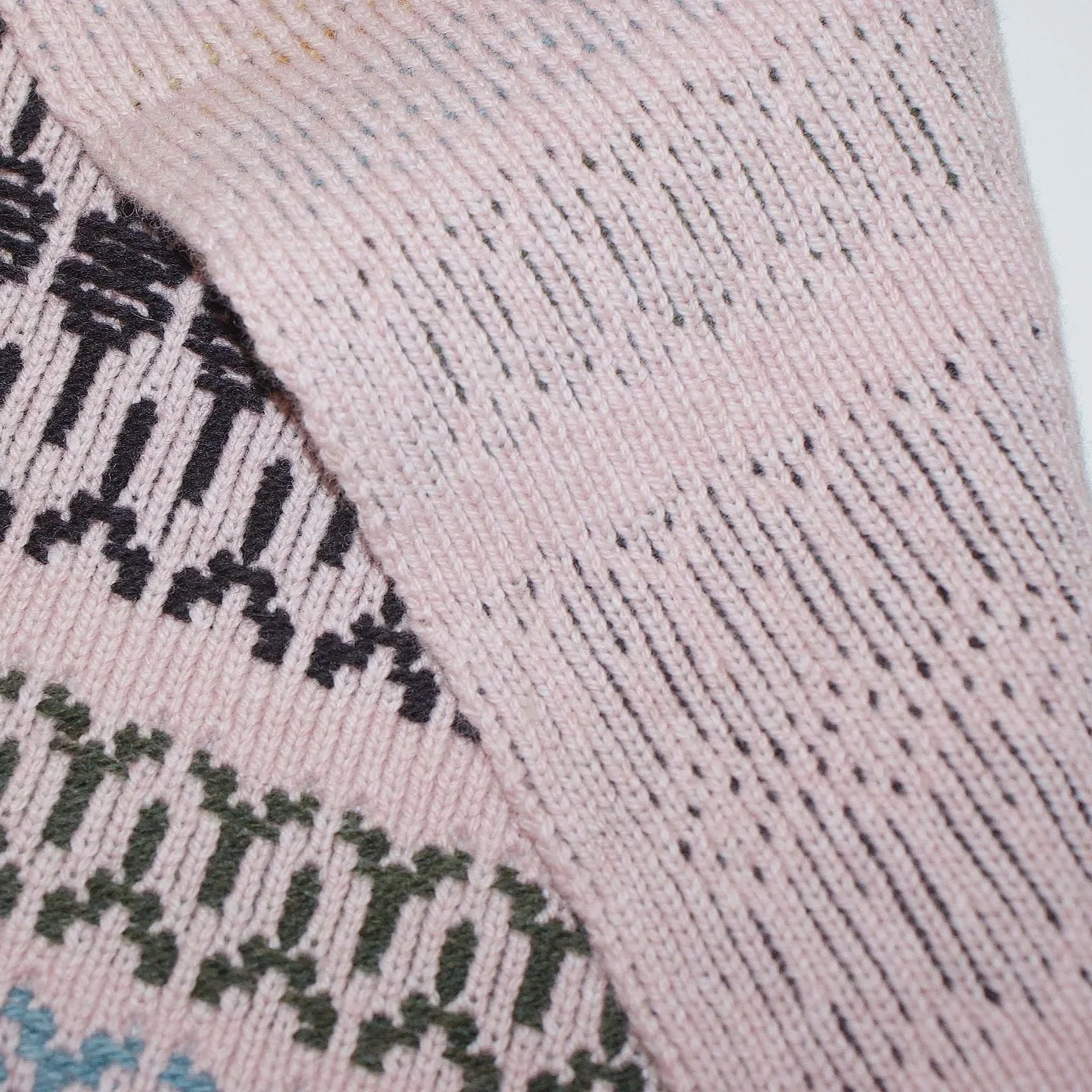 Close-up of knitted fabric with pink, black, blue, and green yarns, patterned with horizontal stripes and small geometric designs.