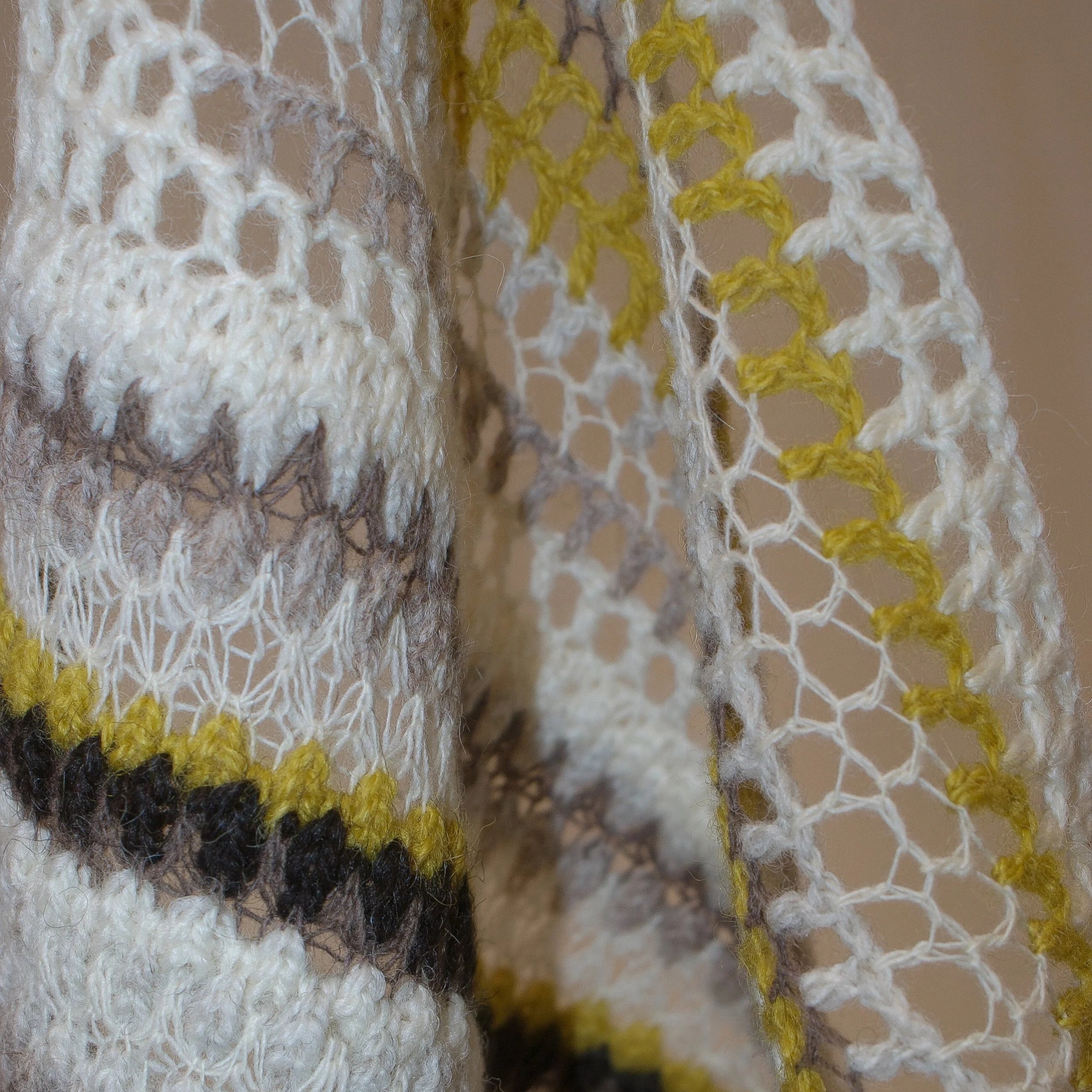 Close-up of a knitted and crocheted textile with white, gray, yellow, and black threads creating a pattern.