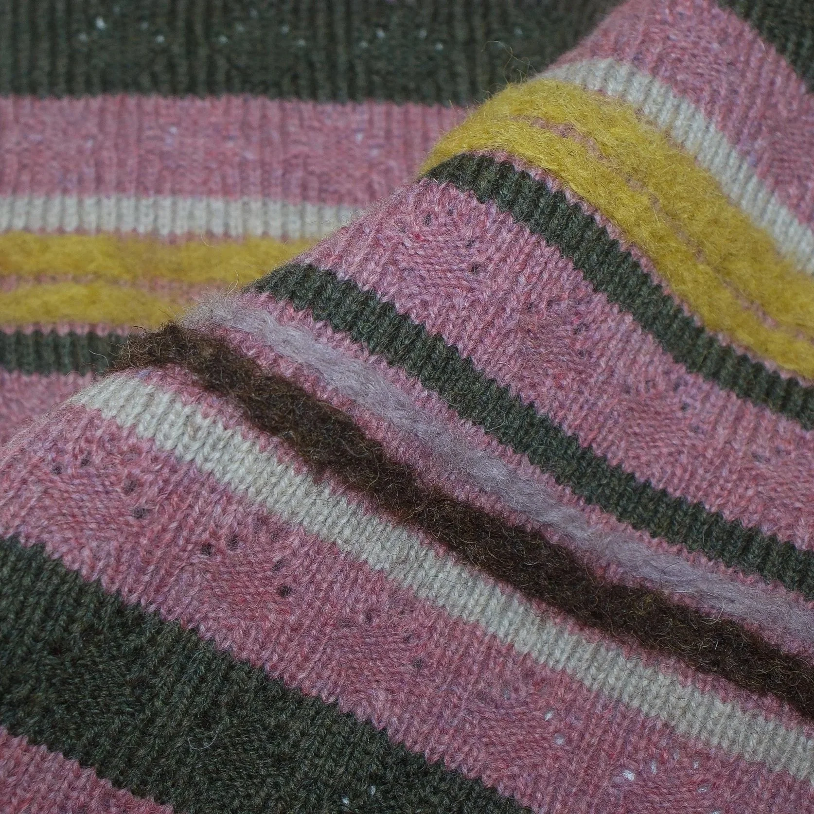 Close-up view of knitted fabric with felted pink, yellow, white, black, and brown stripes.
