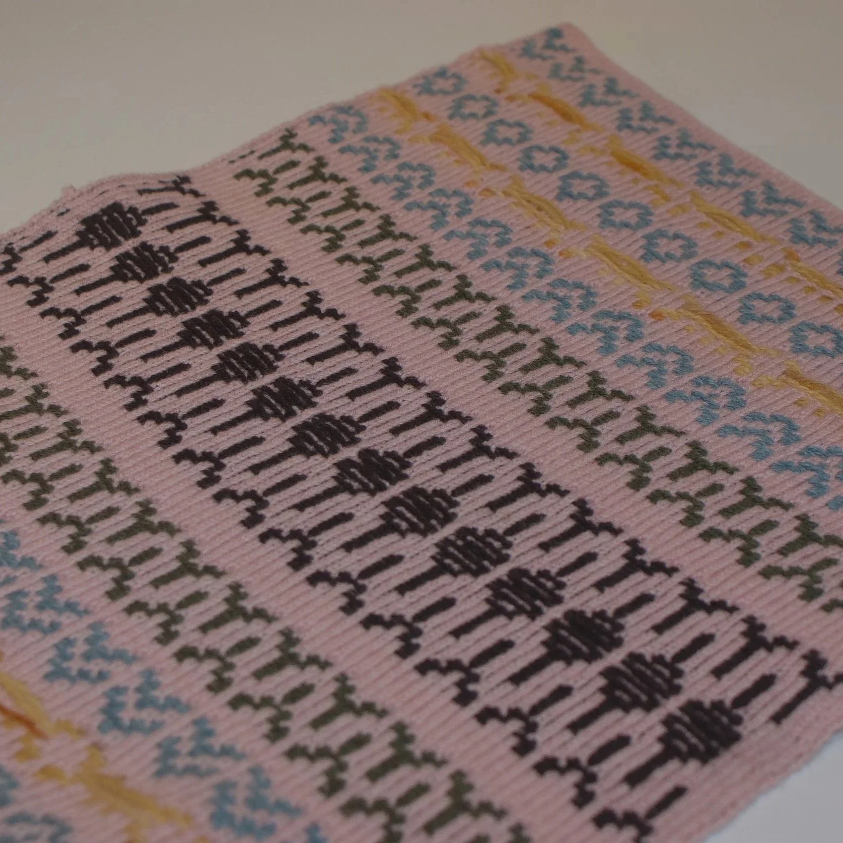 Close-up of a pink fabric with multicolored embroidered patterns.