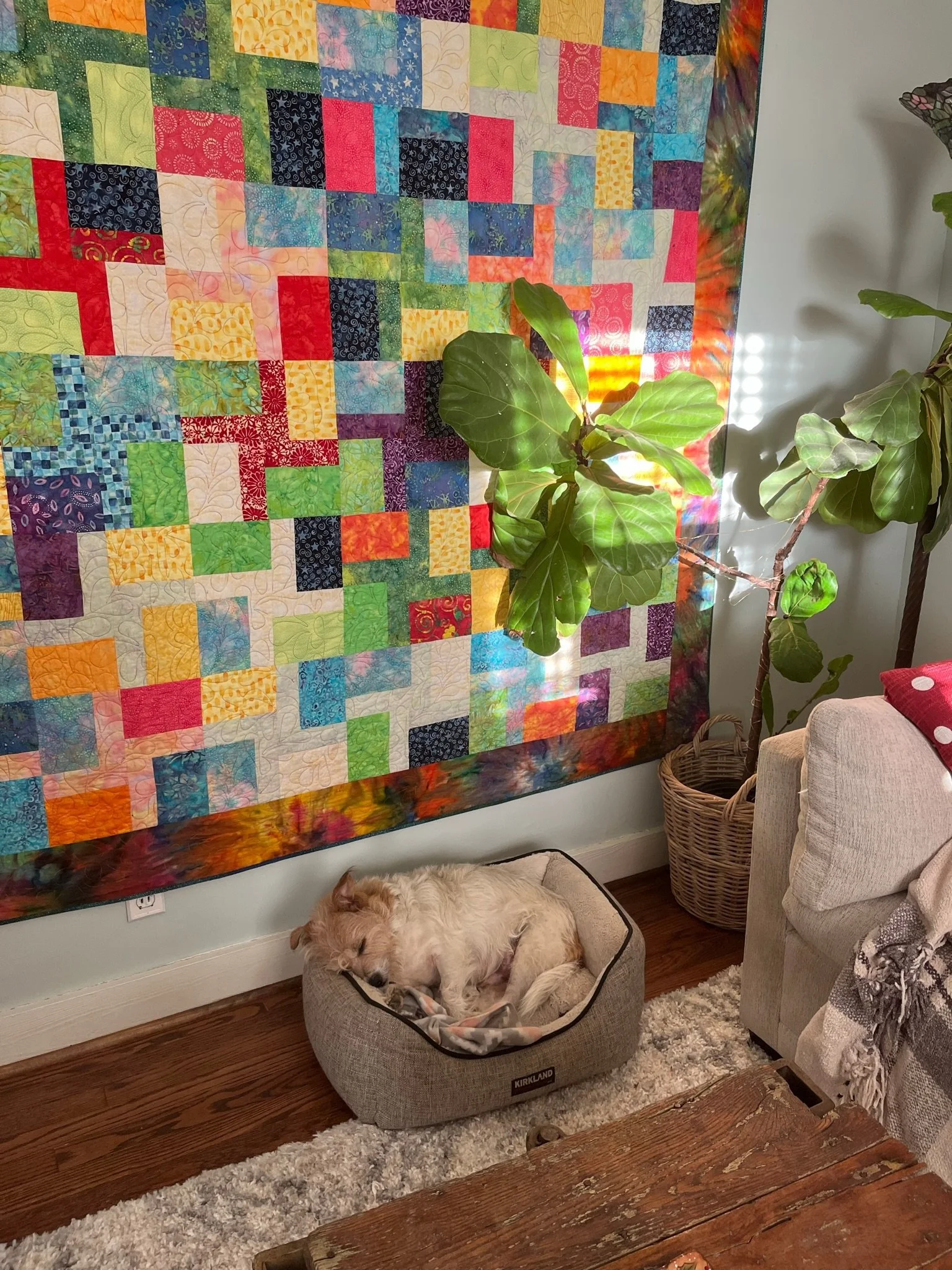 A cozy living room corner featuring a colorful patchwork quilt hanging on the wall