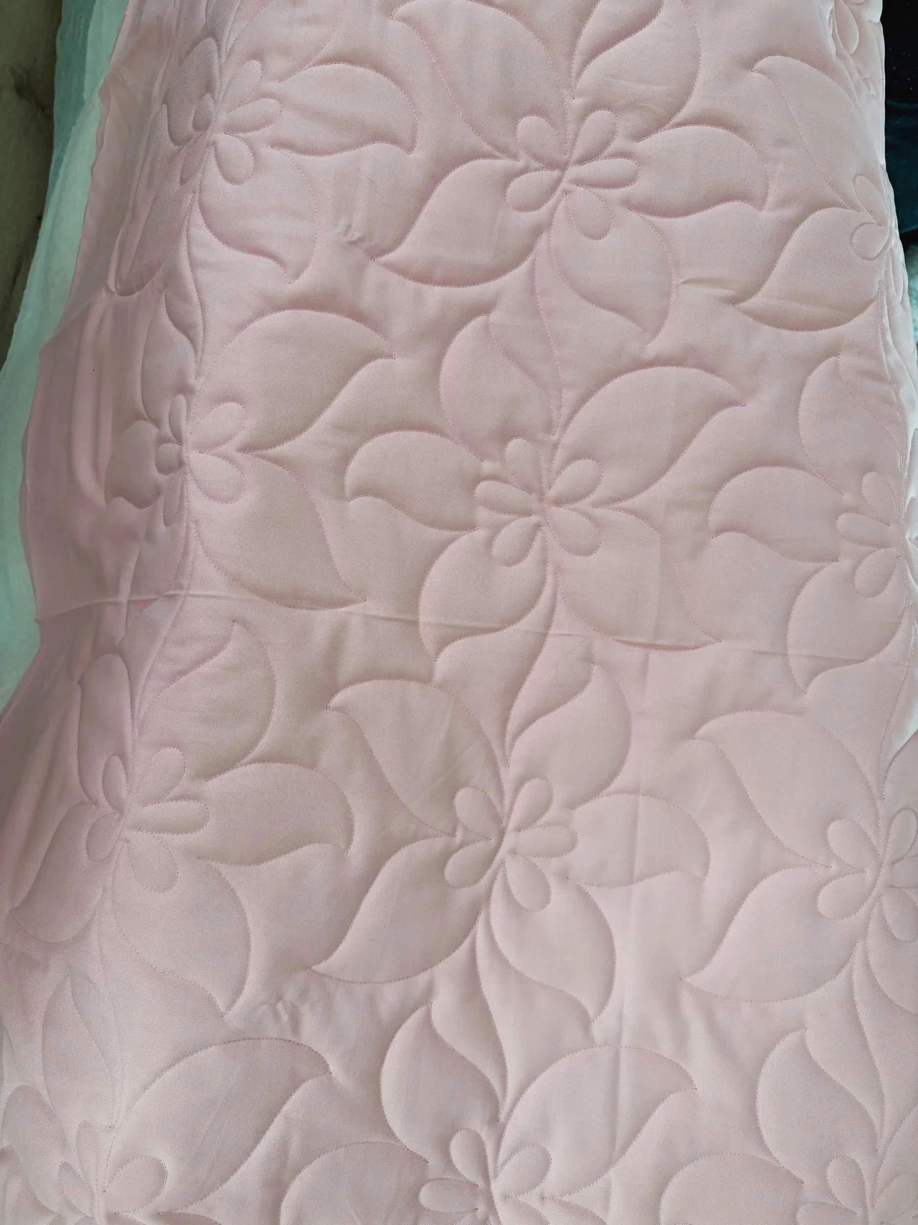 Close-up view of a pink quilted fabric with floral pattern stitching
