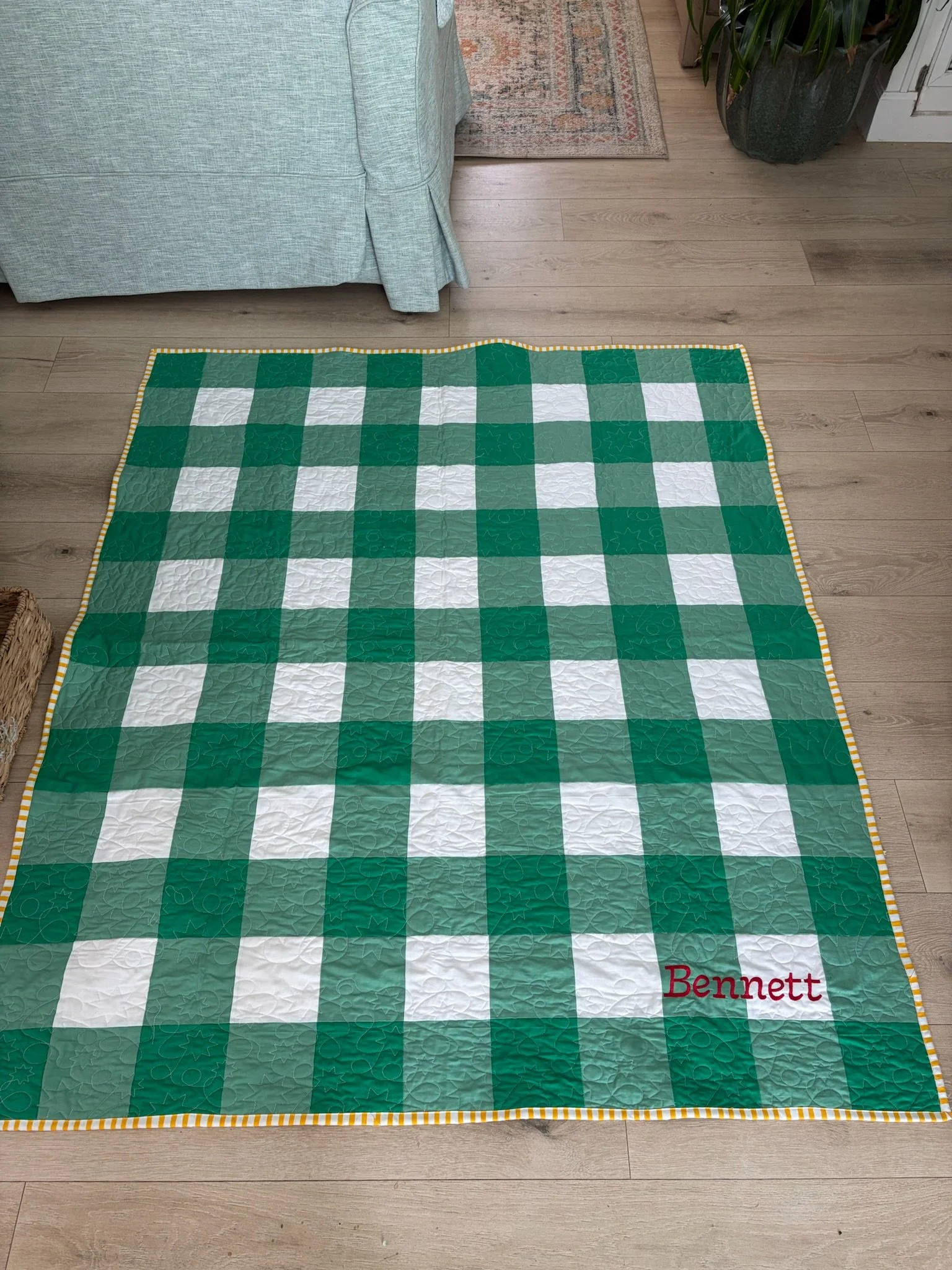 A green and white checkered quilt with a yellow and white striped border, personalized with red embroidered text reading 'Bennett'
