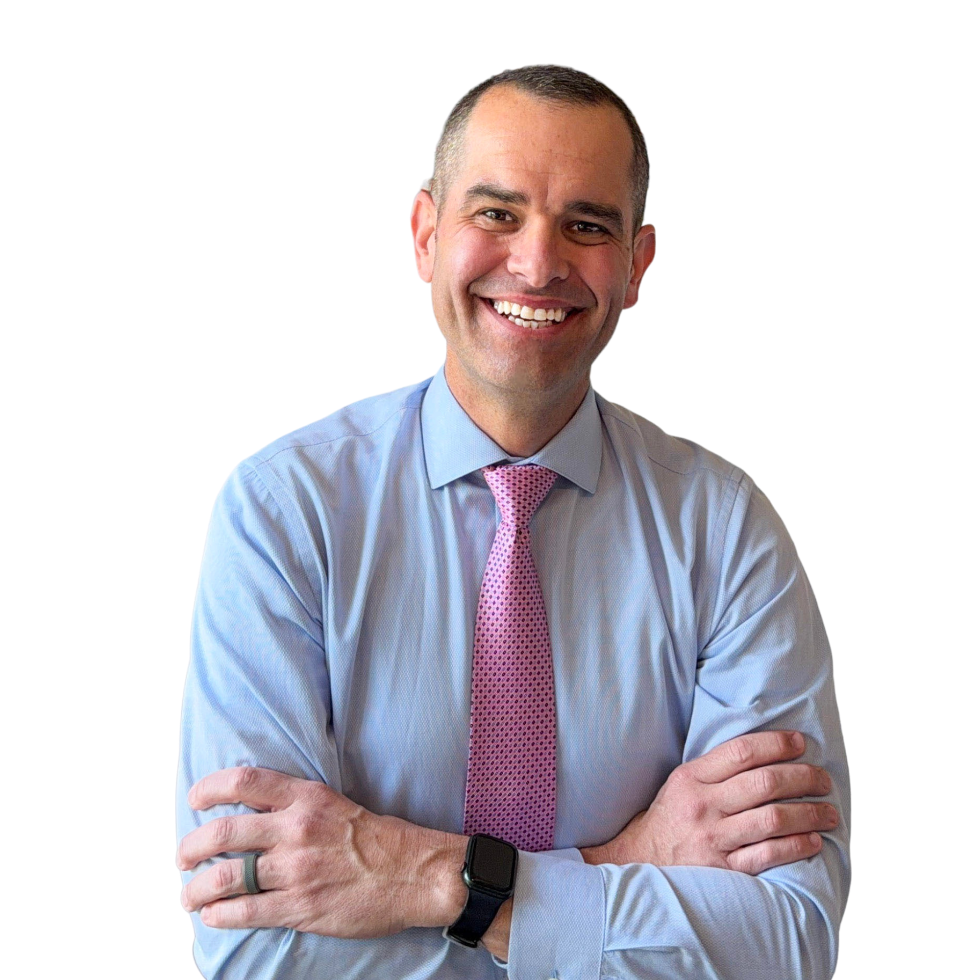A man wearing a light blue shirt, pink patterned tie, and smartwatch, smiling with arms crossed, standing against a black background.