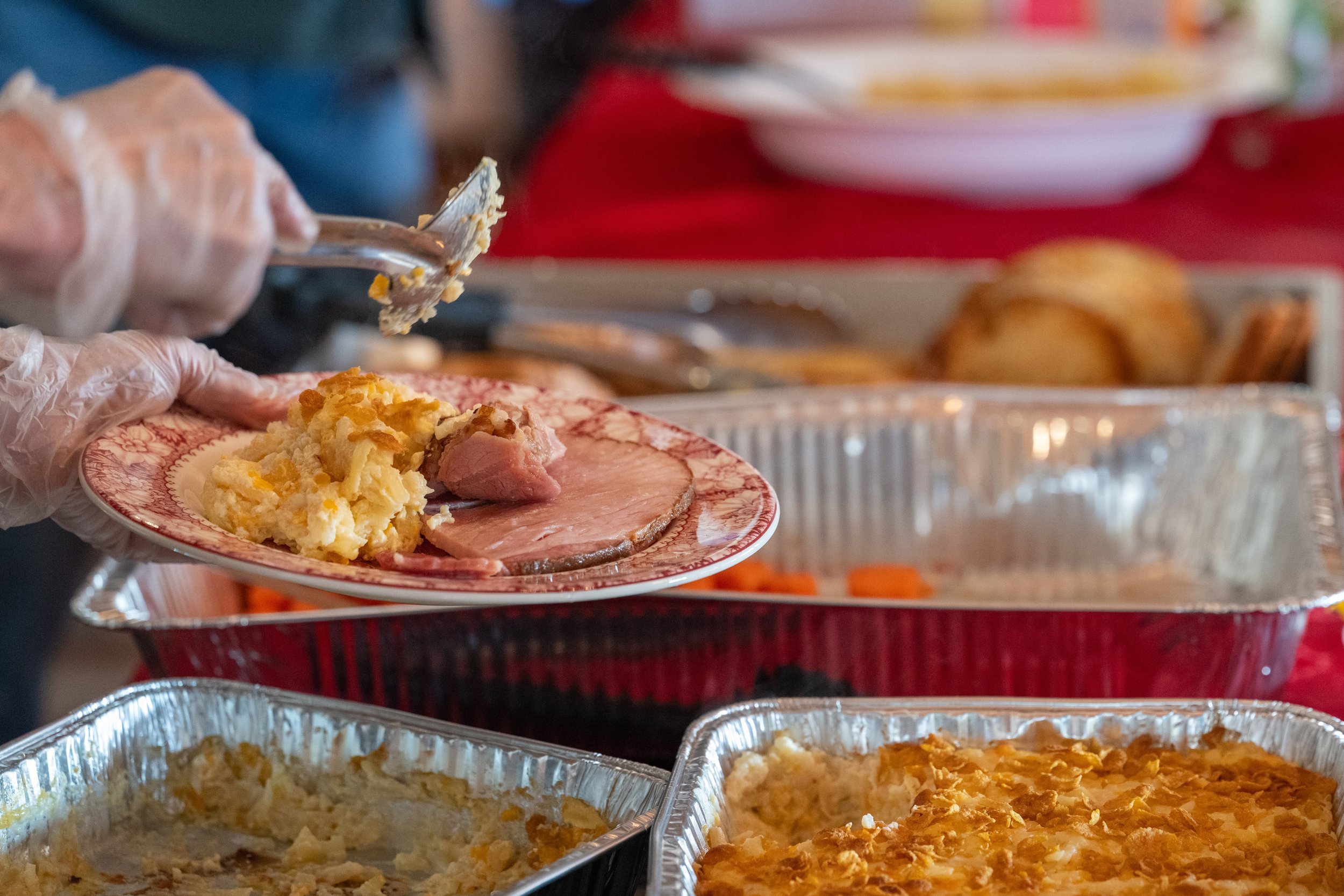 Gloved server plating sliced ham and casserole at a buffet dinner.