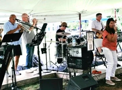 Live band performing under a tent with singers, guitarists, brass players, and a drummer