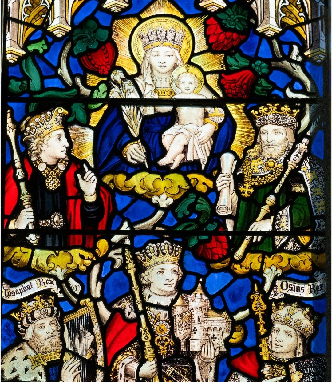Decorative stained-glass window depicting the Virgin Mary and Christ child surrounded by crowned medieval kings, heraldic symbols, and floral motifs