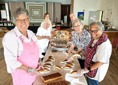 Group of women wearing aprons preparing and packaging freshly baked bread in a community kitchen
