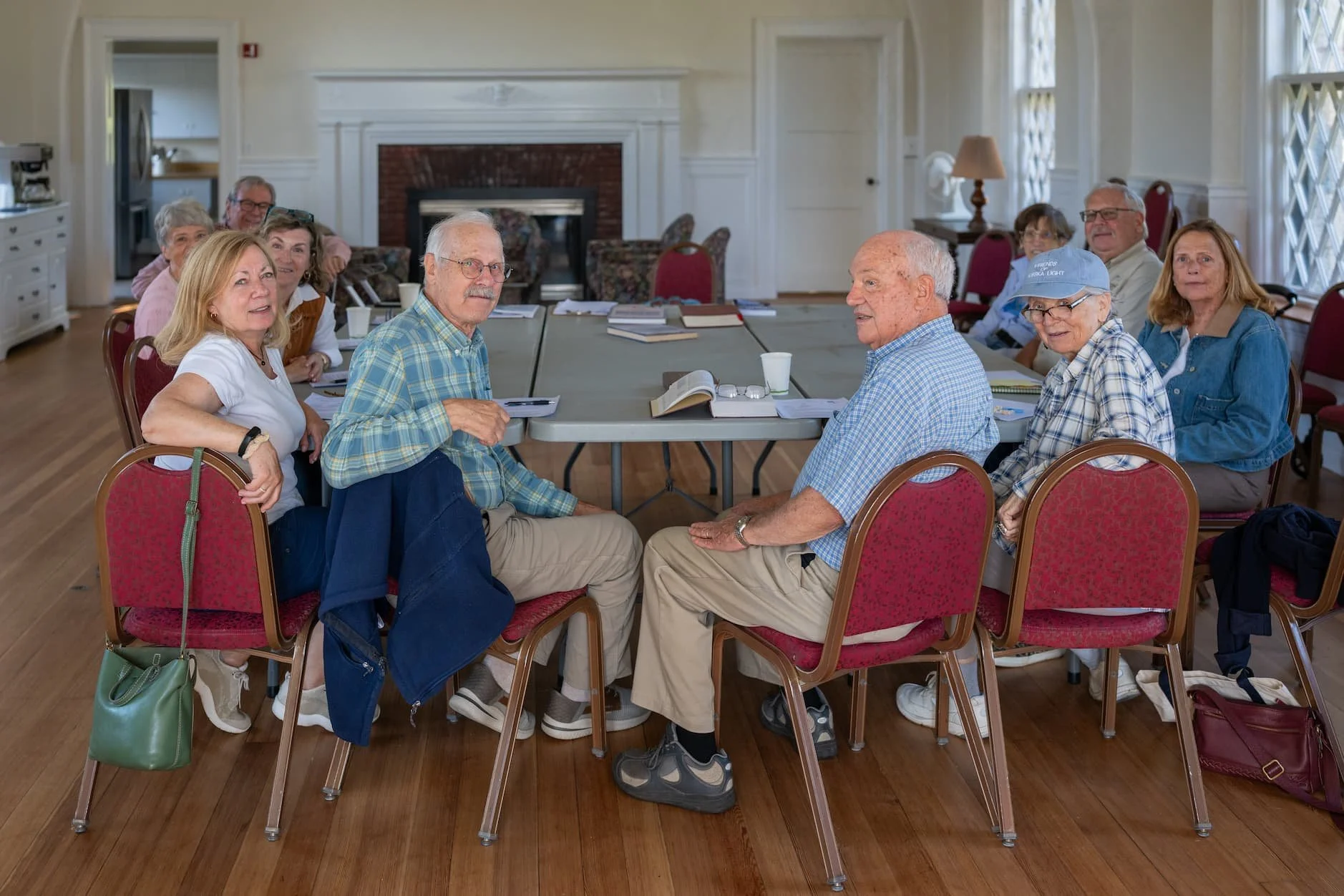Group of older adults seated around tables in a bright room with a fireplace and large windows