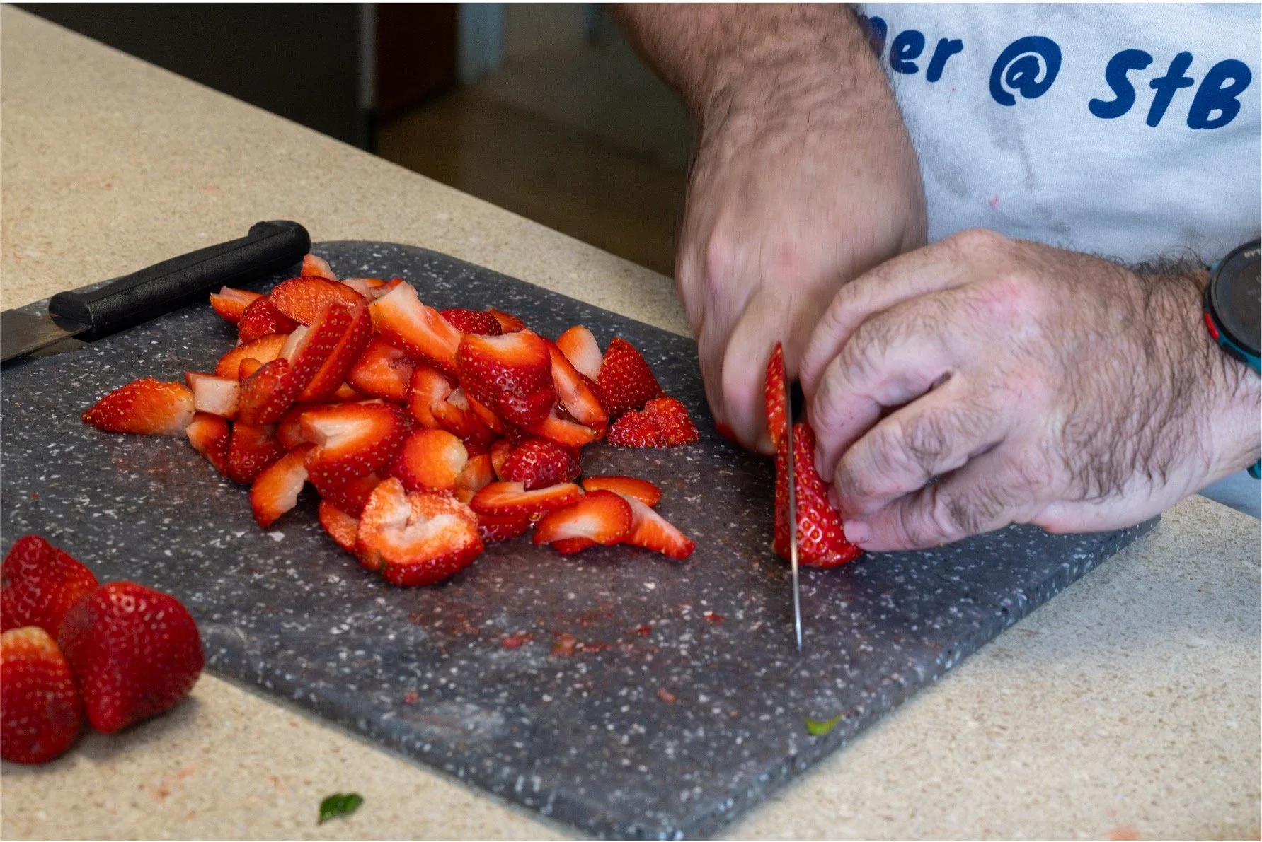 Person slicing strawberries on a black cutting board with a kitchen knife