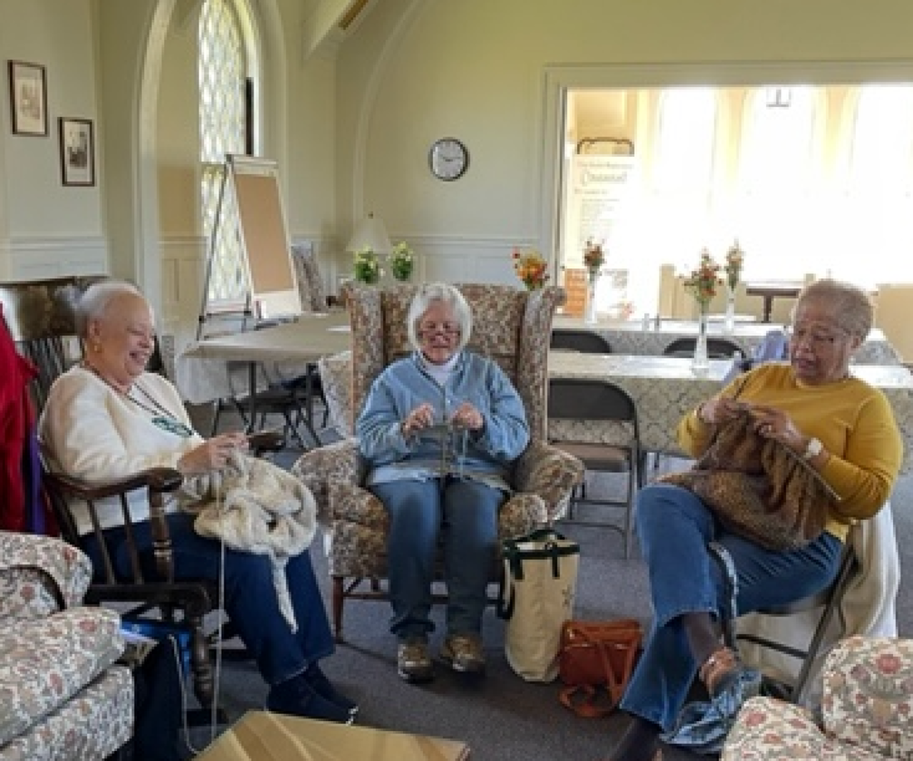 Three older women knit together in a bright community room.