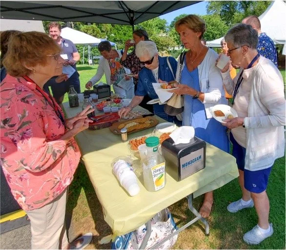 People serving and enjoying food at an outdoor community gathering under a canopy