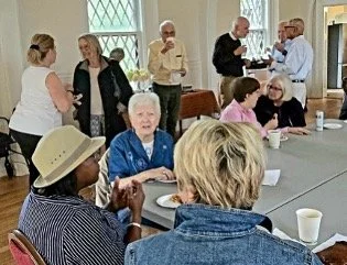 Group of parishioners socializing after the service with some standing and some seated at tables.