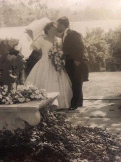 Vintage black-and-white wedding photo of a bride and groom kissing beside a flower-filled fountain in a garden.