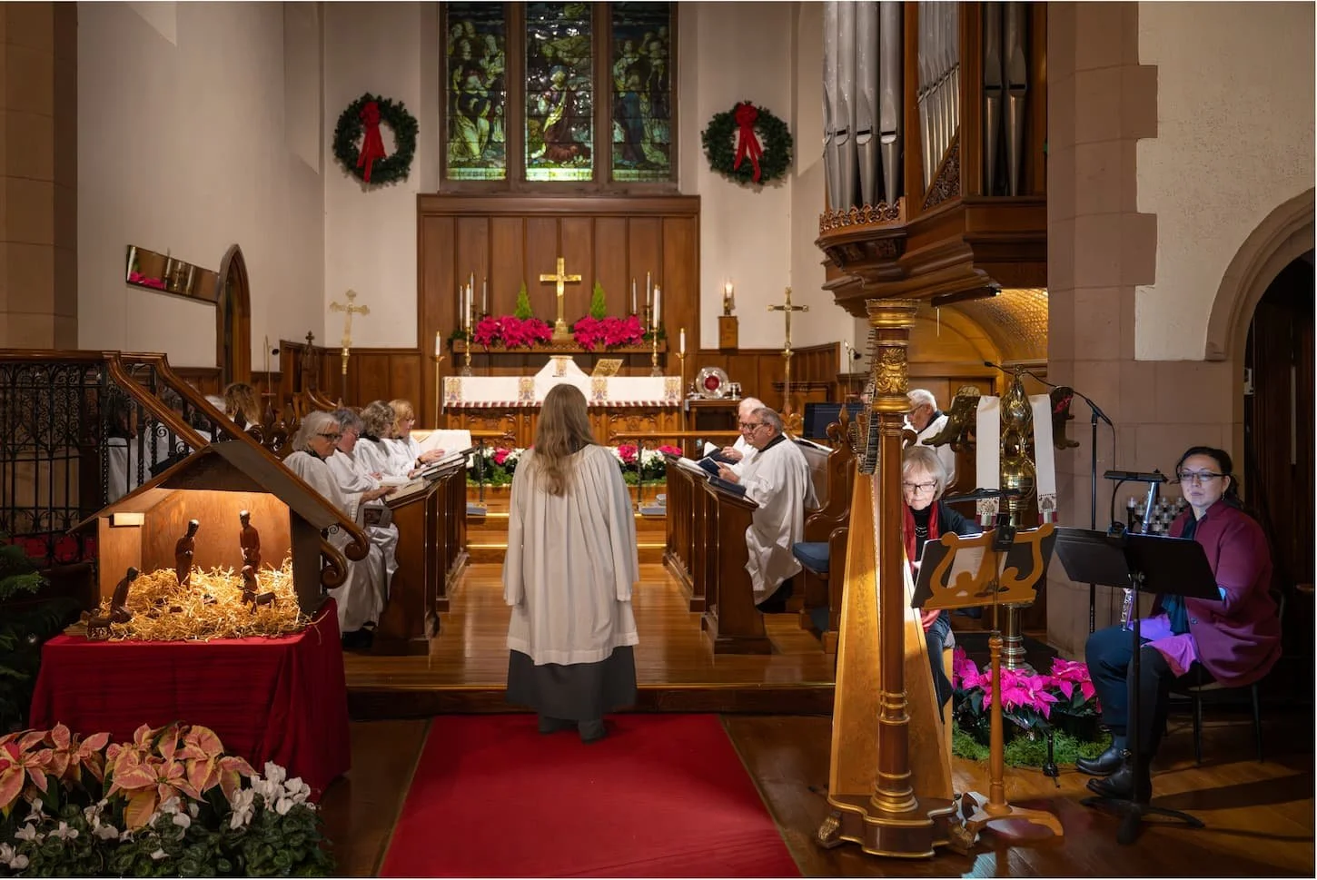 Christmas church service with choir, altar, nativity scene, stained-glass window, organ, and harpist