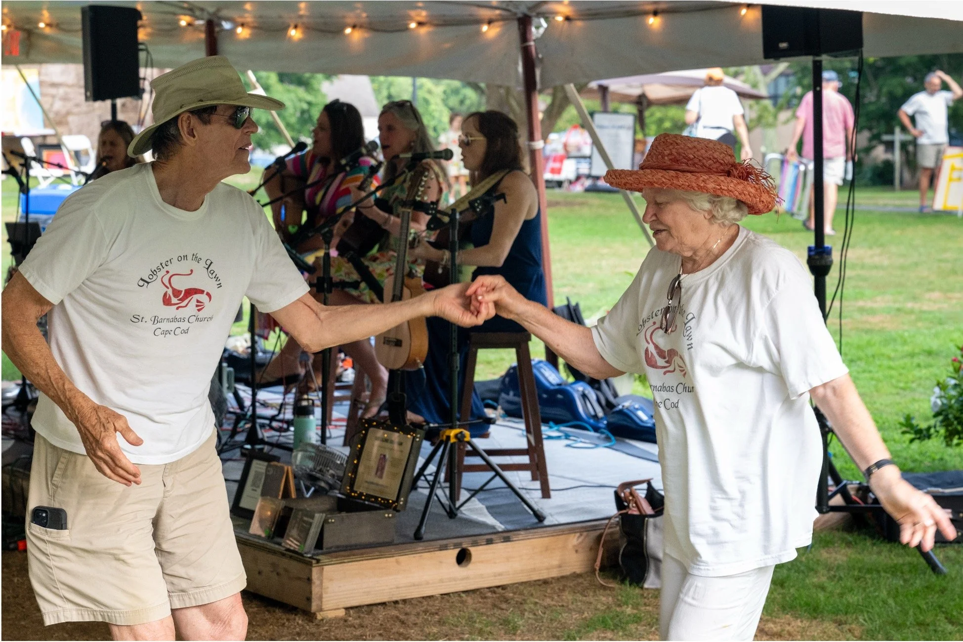 Two people dance in front of a live band performing under an outdoor tent at a community event.