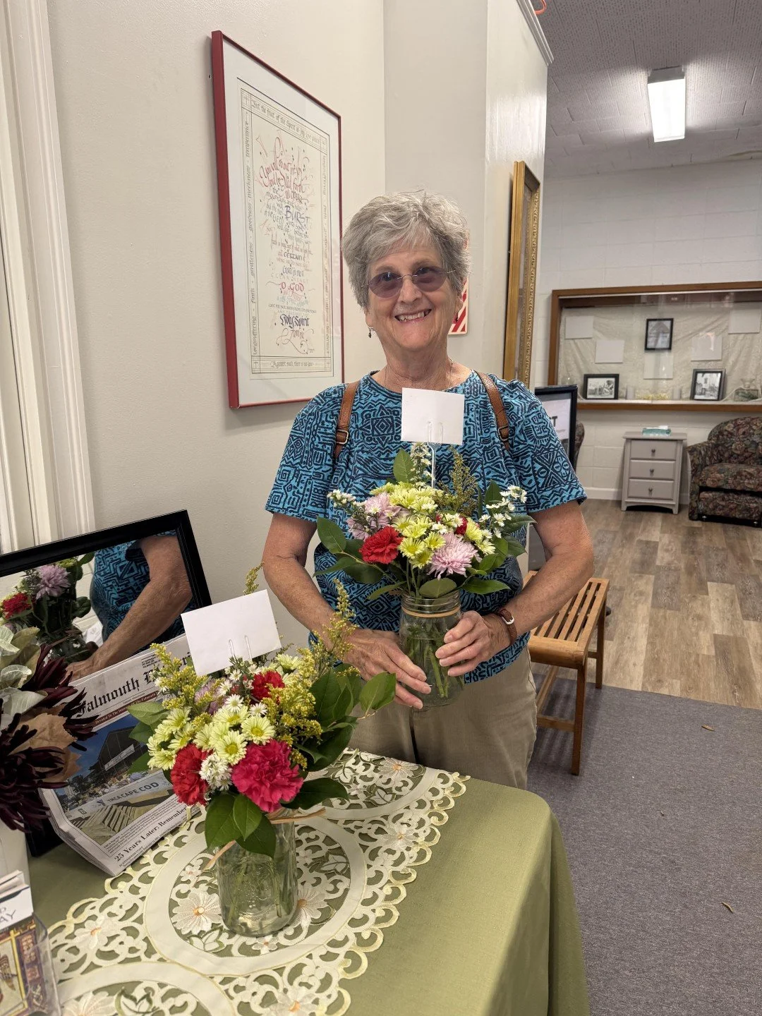 Smiling older woman holding a colorful bouquet of flowers in a community room