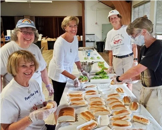 Volunteers prepare sandwiches at a community food event, arranging bread rolls and fillings on a long table.