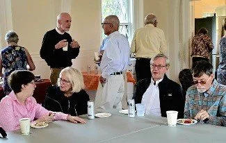 Group of adults socializing and eating at tables during an indoor gathering.