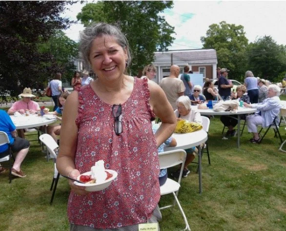 Smiling woman holding a plate of dessert at an outdoor community picnic