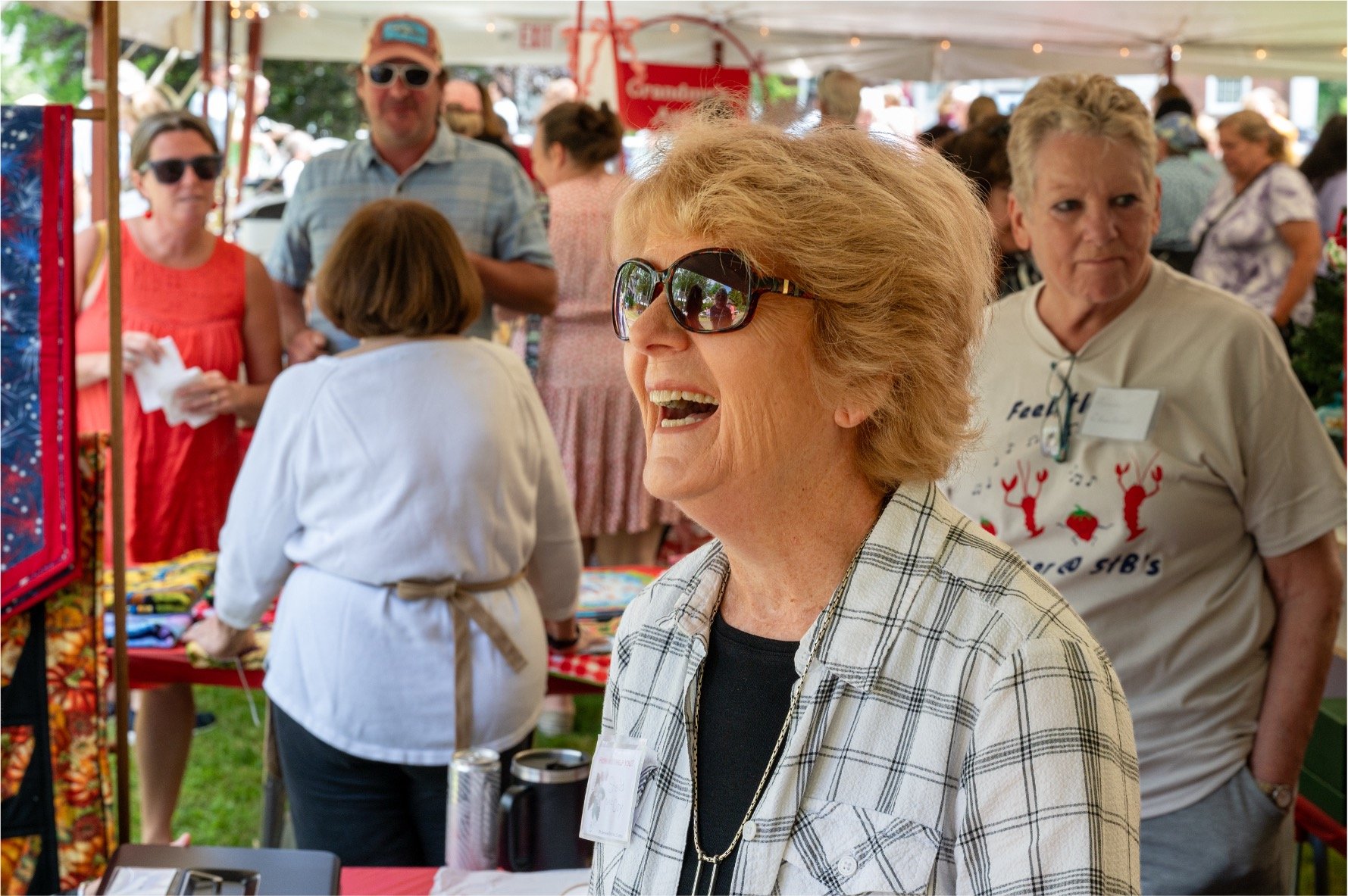 Smiling woman wearing sunglasses at a crowded outdoor community event