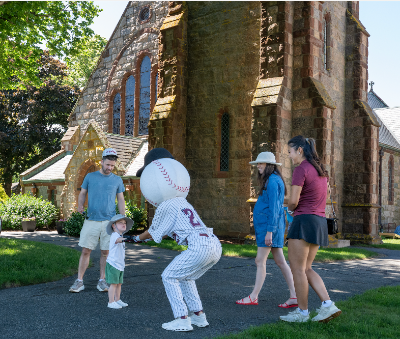 Baseball mascot entertaining a child and family outside a historic stone church.