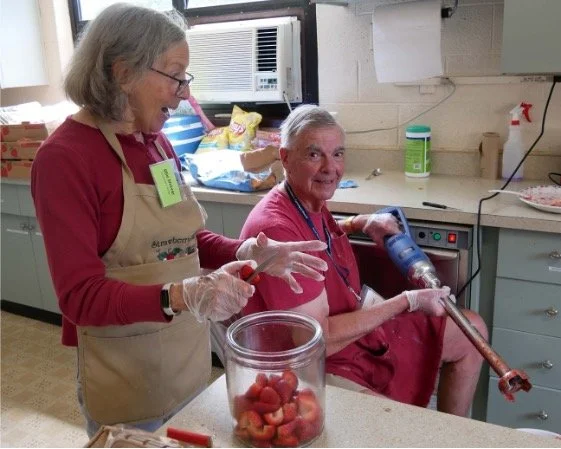 Volunteers in aprons prepare strawberries in a community kitchen