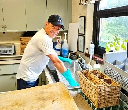 Restaurant worker wearing gloves washes dishes at a commercial kitchen sink.