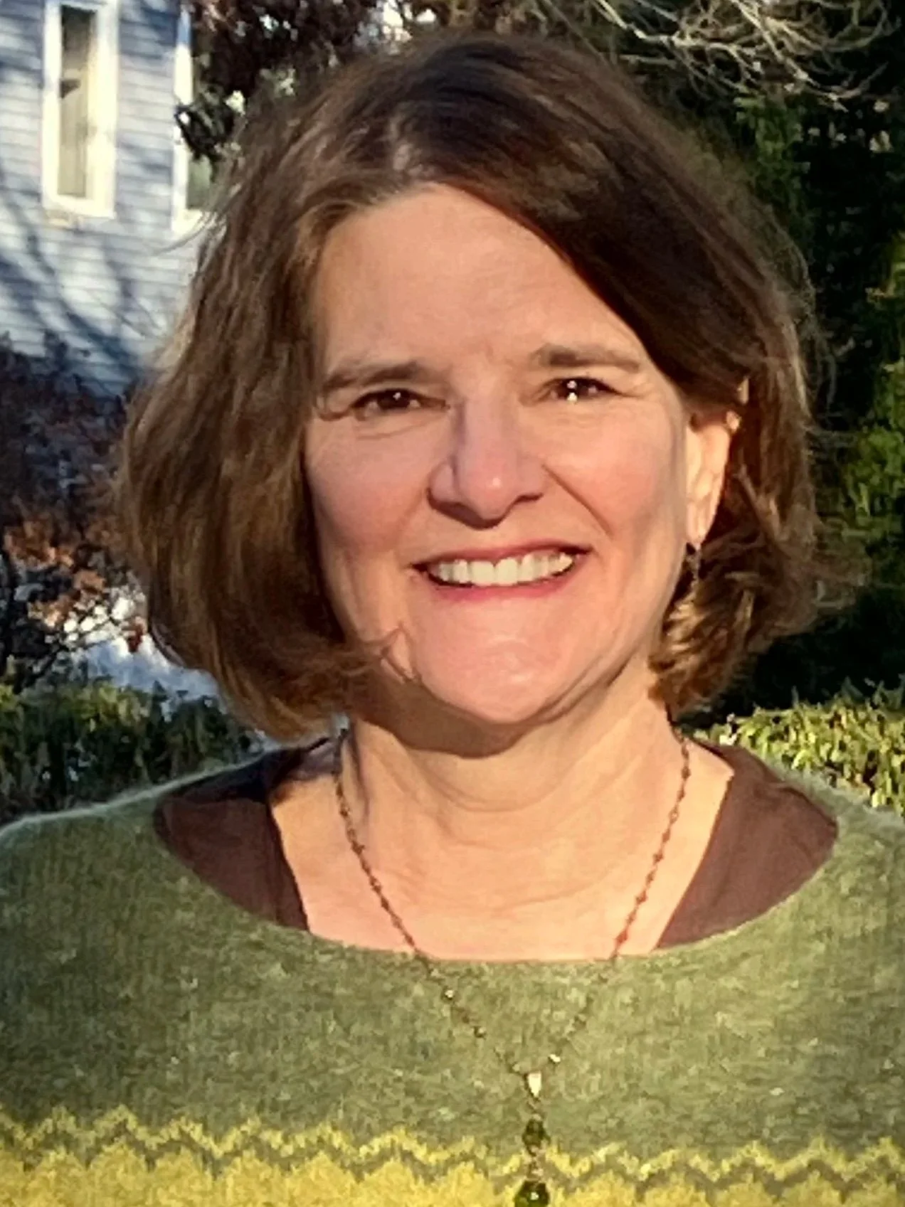 Smiling woman with shoulder-length brown hair wearing a green sweater outdoors