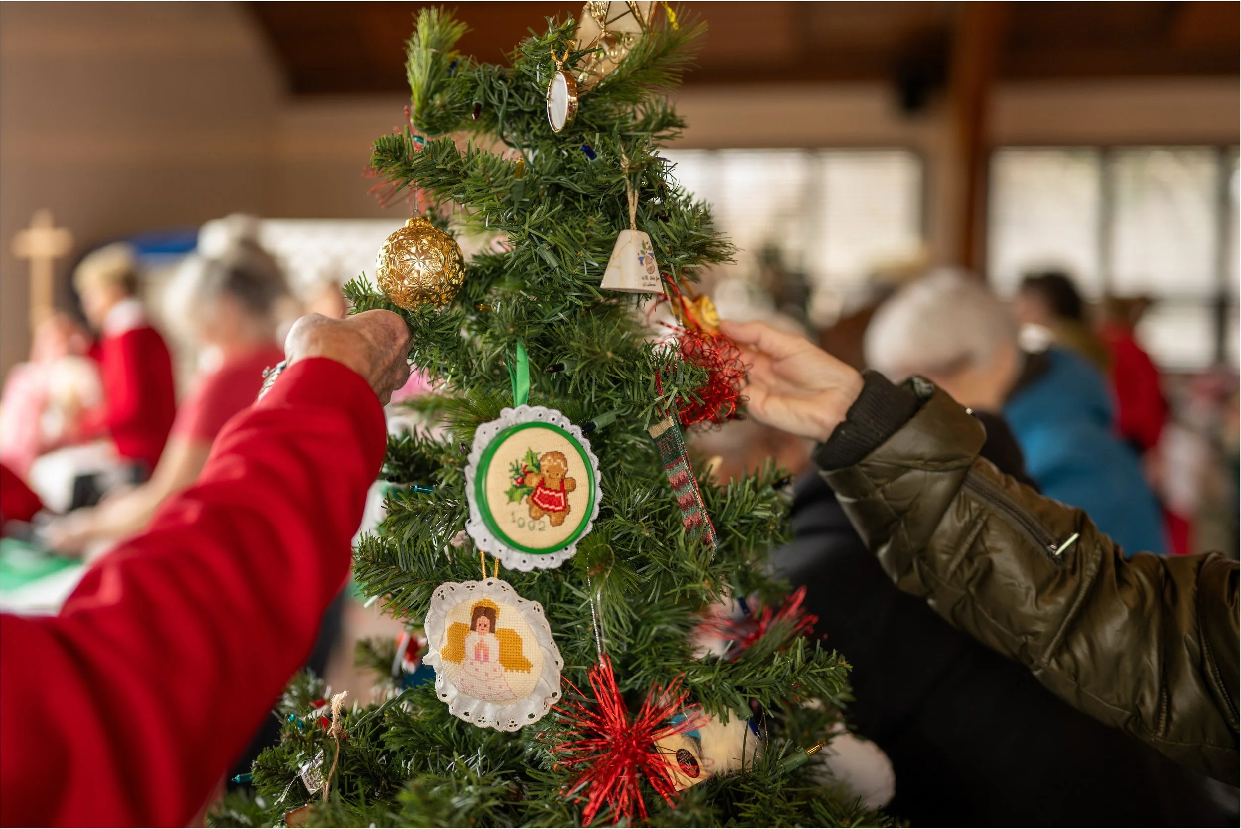 People decorating a Christmas tree with handmade ornaments in a festive indoor setting