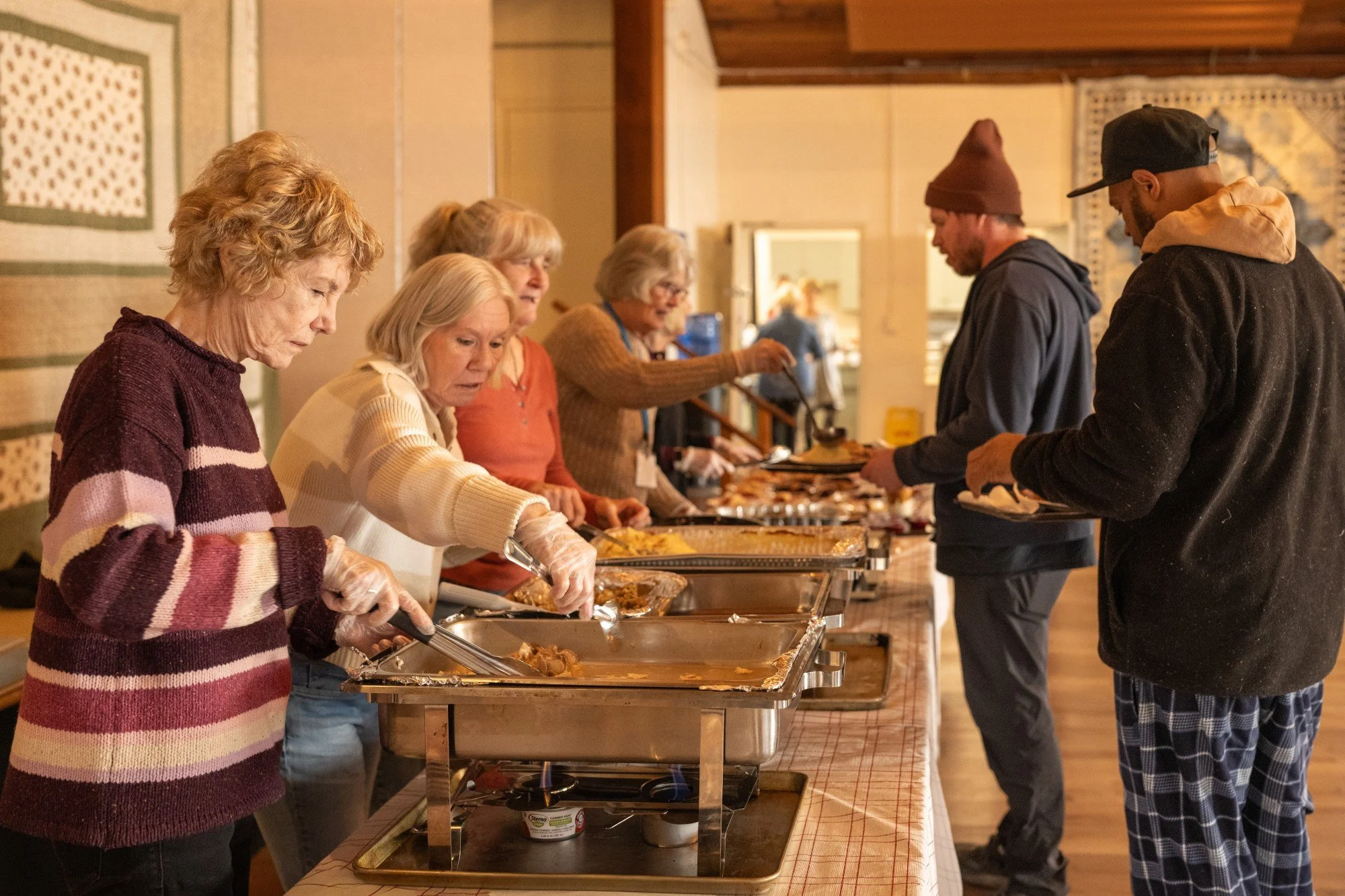 People serving and receiving food at a community buffet table