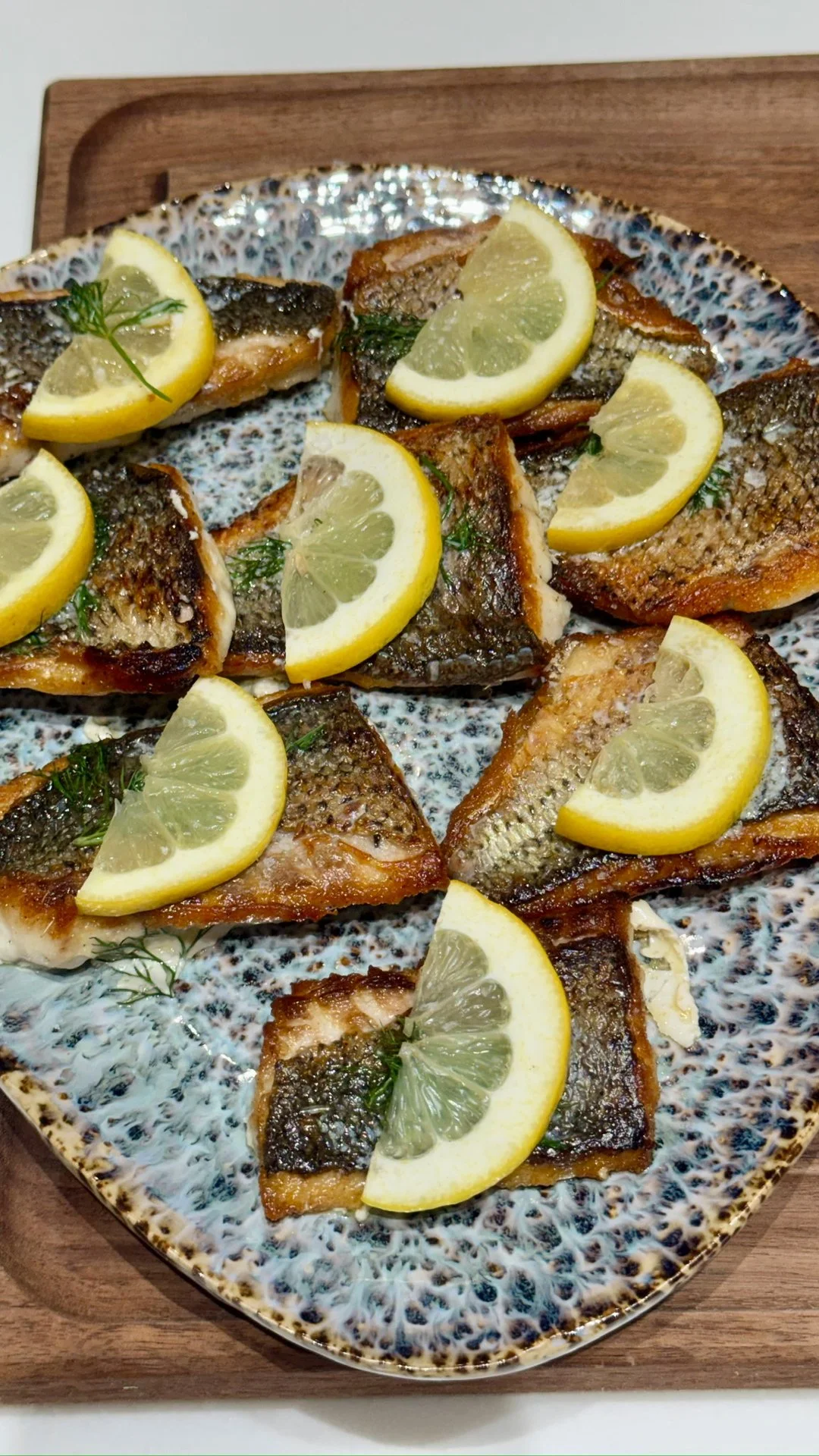 Sliced grilled fish topped with lemon wedges and garnished with herbs on a decorative ceramic plate.