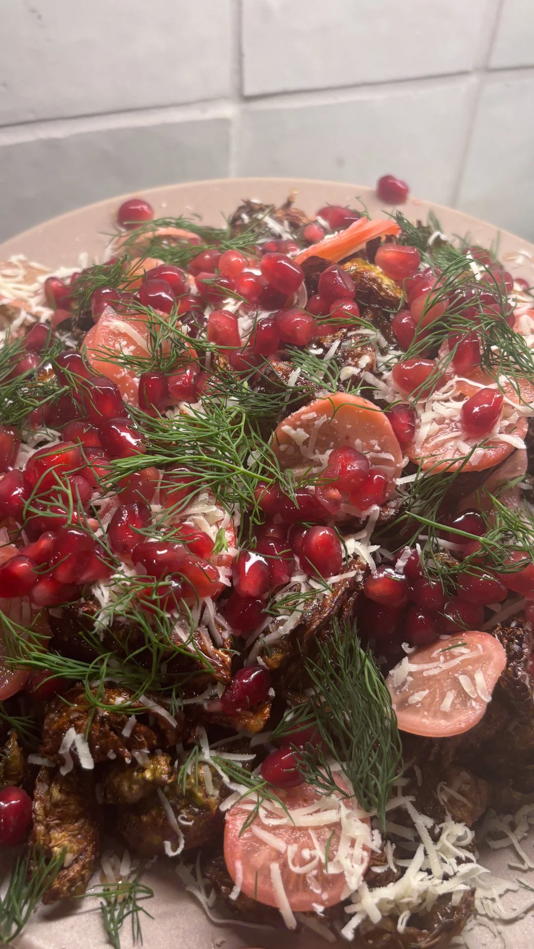 A plate of food featuring pomegranate seeds, dill, sliced tomatoes, shredded cheese, and cooked vegetables.