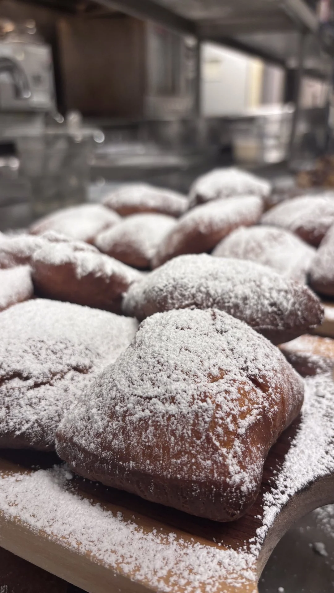 Close-up of baked cookies dusted with powdered sugar on a wooden board in a kitchen.