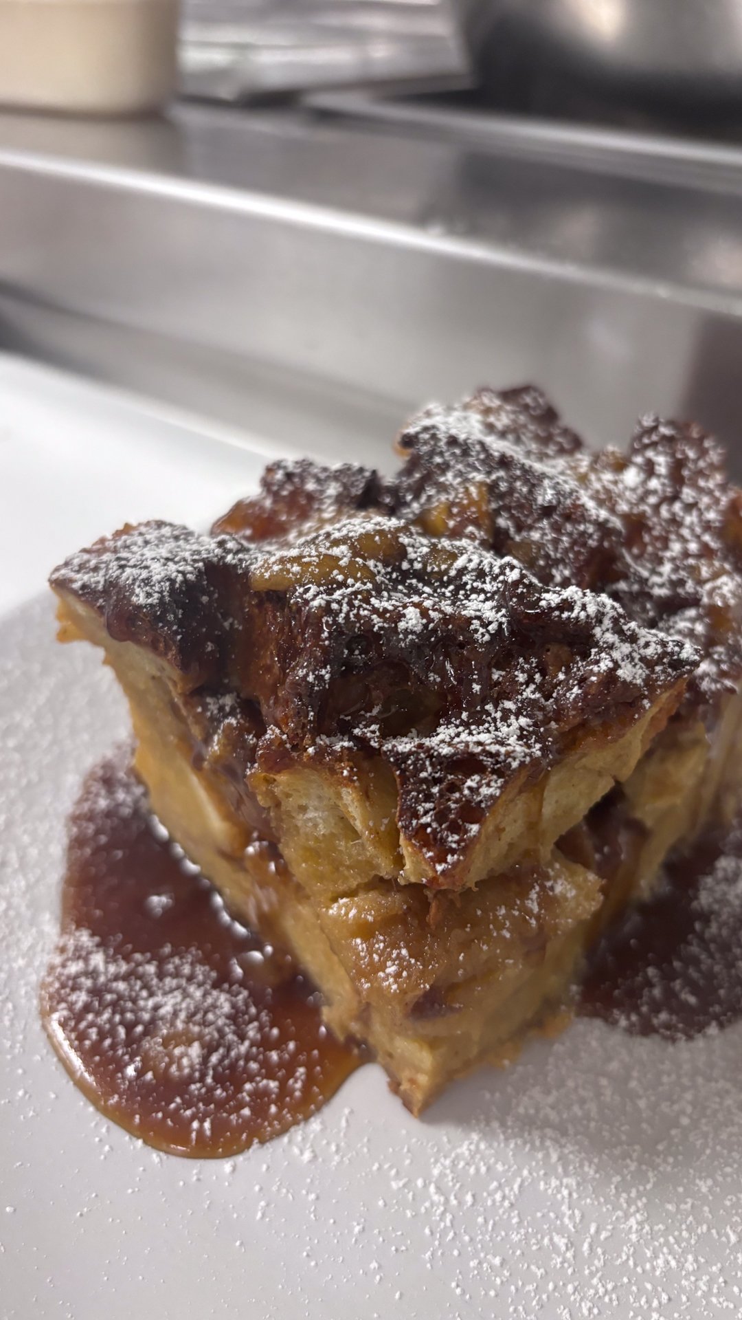 A piece of apple cobbler topped with powdered sugar and drizzled with caramel sauce, on a white plate.