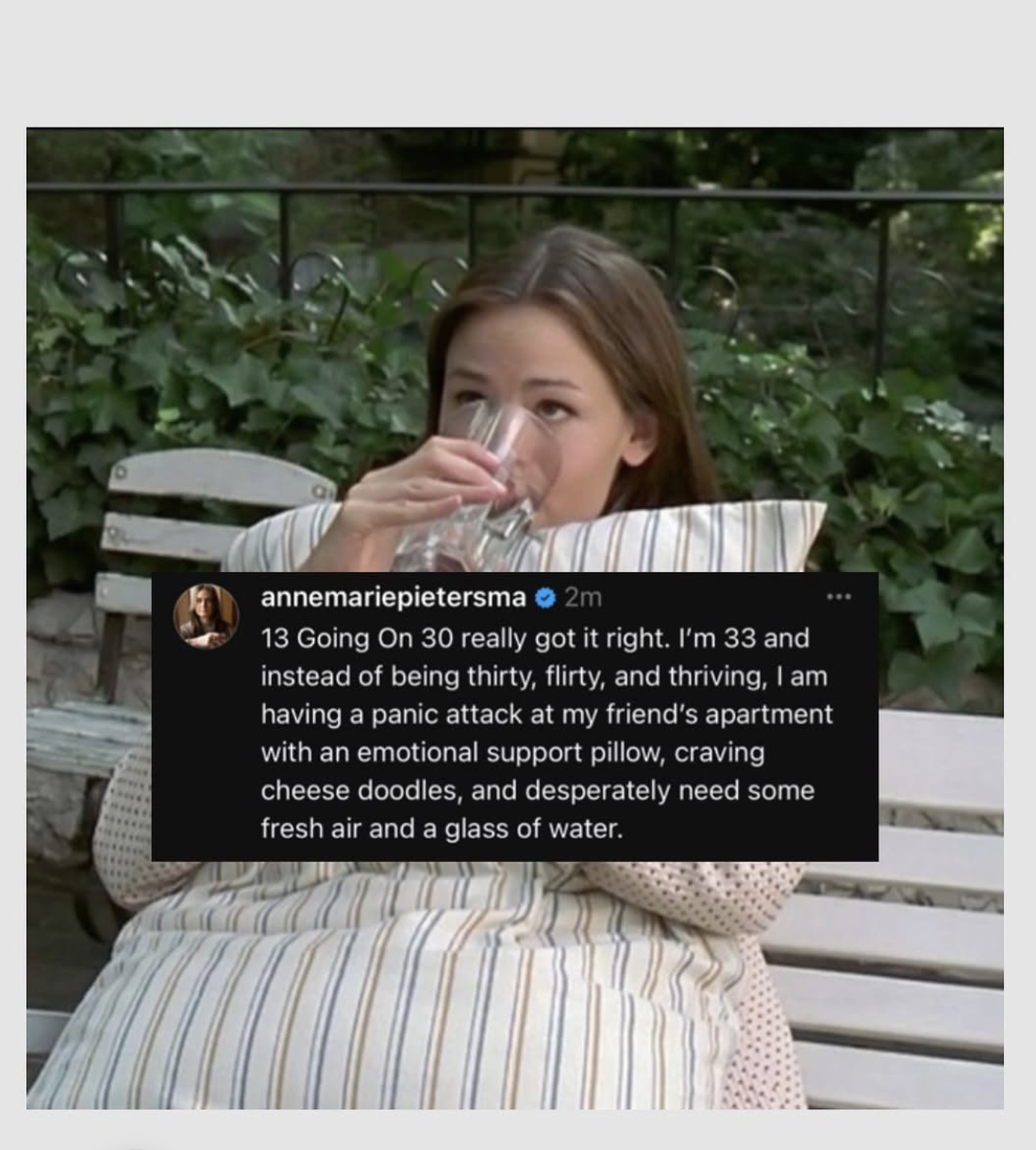 A woman with brown hair is sitting outdoors on a bench, drinking from a glass of water, surrounded by green foliage. There is a social media comment overlayed on the image.