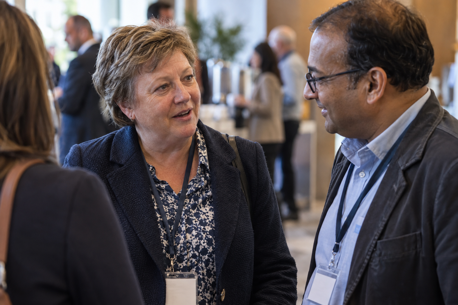 Three people engaged in conversation at a professional event, with a woman in the middle speaking and a man and woman listening.
