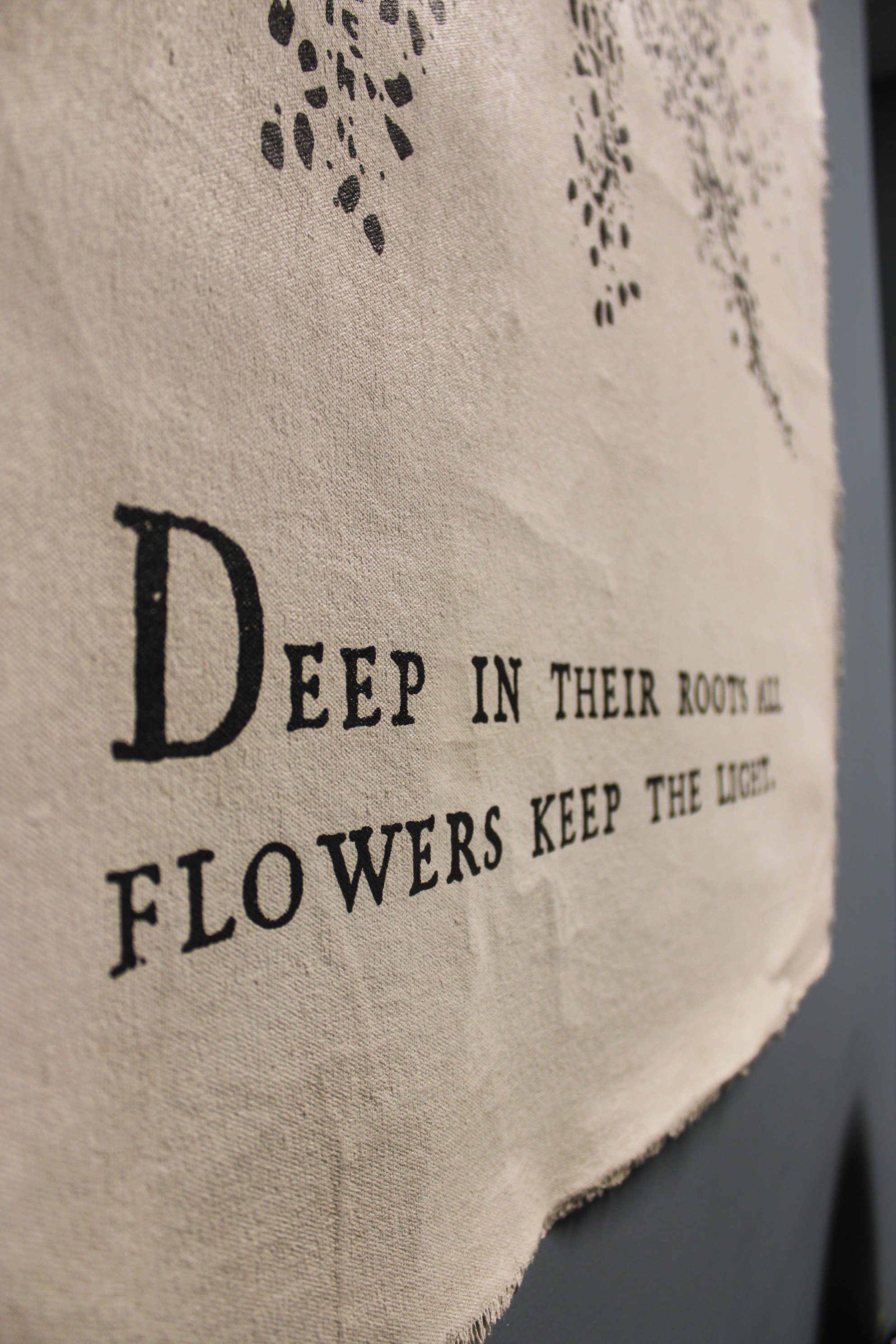 Close-up of a fabric with printed text, featuring decorative black dots and partially visible sentence about flowers and roots.