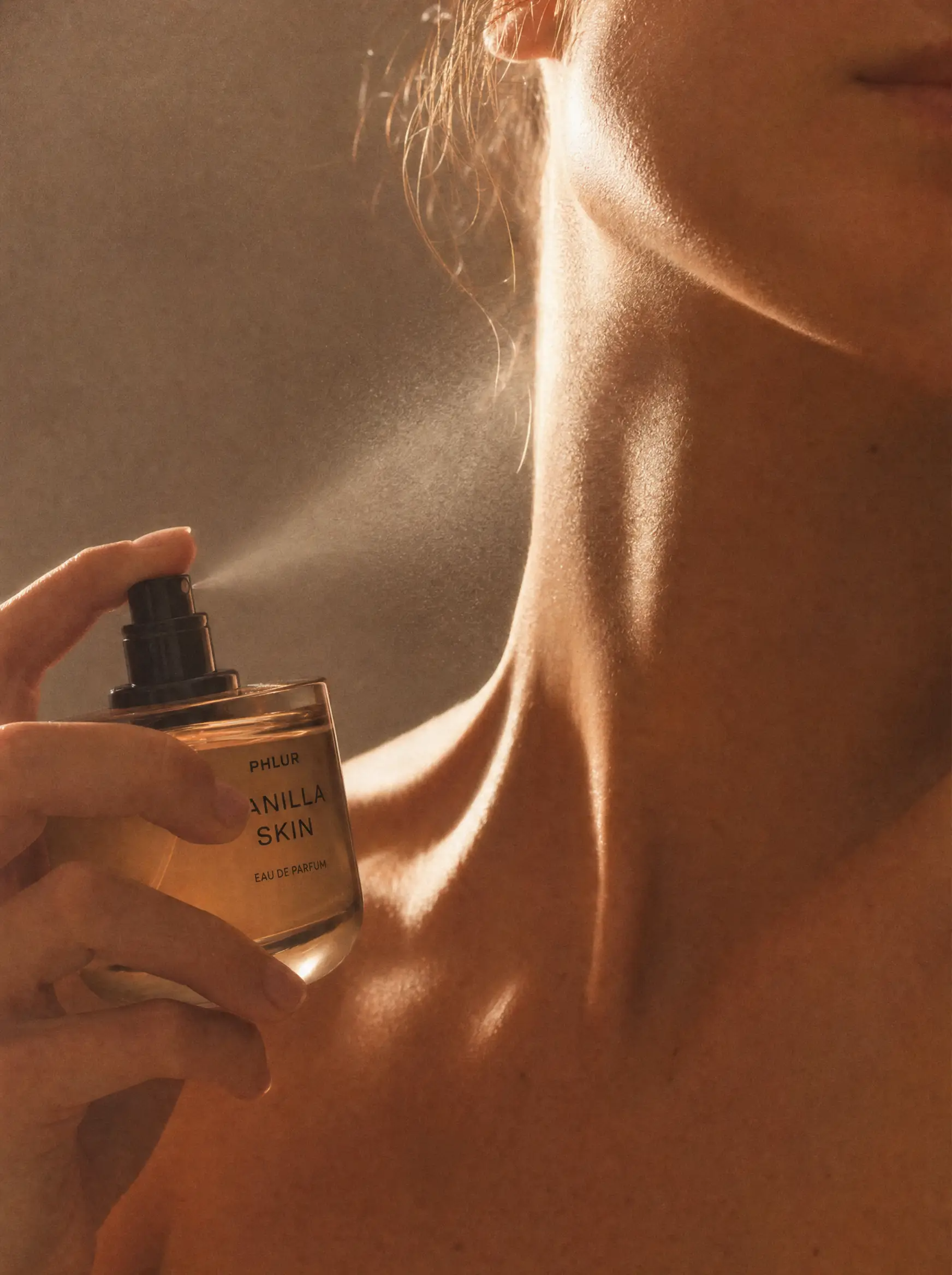 Close-up of a person spraying perfume on their shoulder in warm lighting.