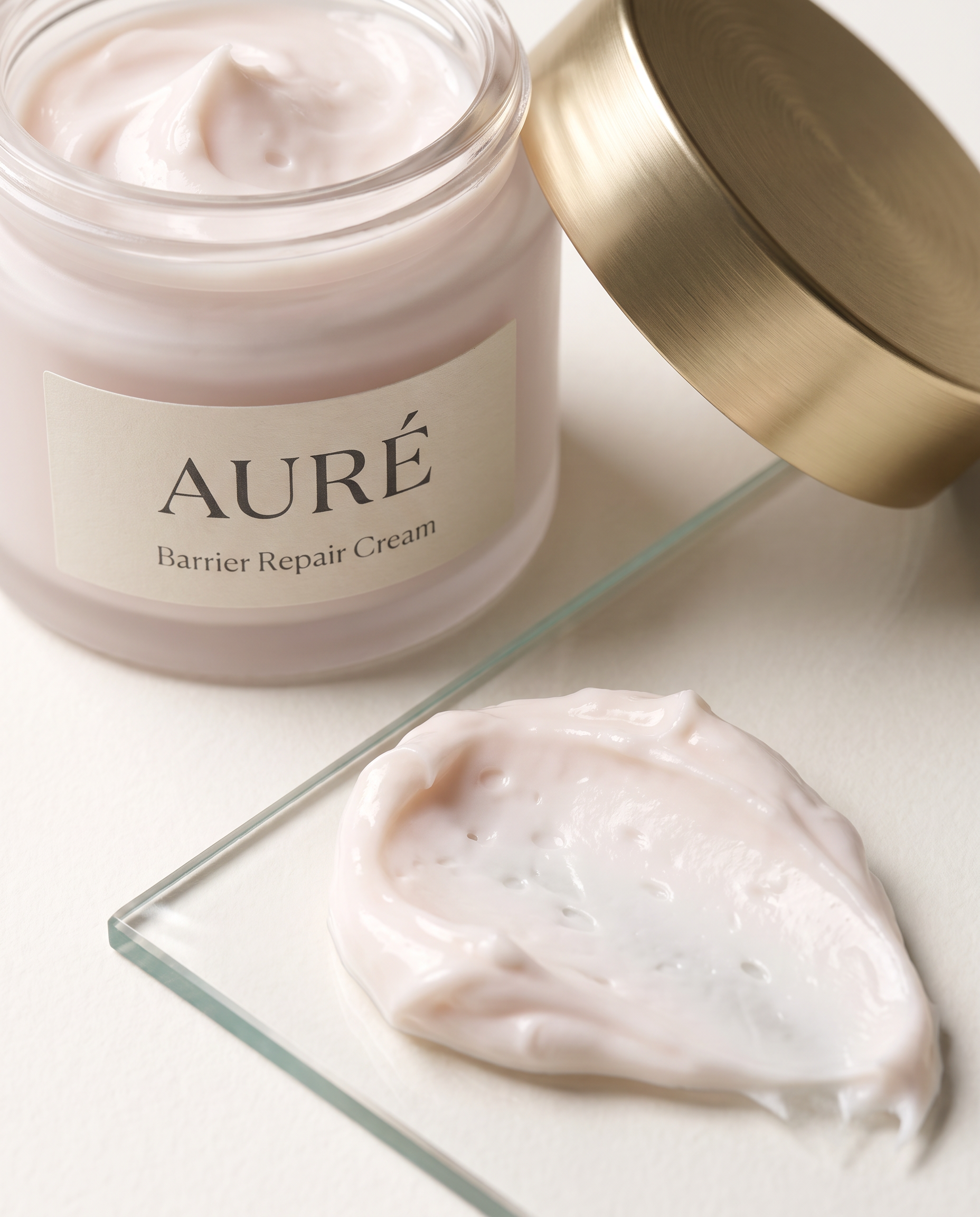 A jar of Aura Barrier Repair Cream with the lid slightly off, revealing the creamy-textured product inside, placed on a glass surface.