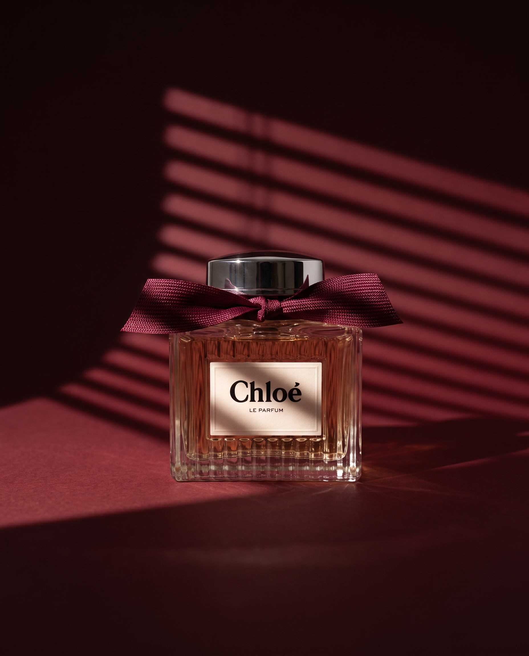 A bottle of Chloe Le Parfum perfume with a dark background, featuring pink lighting and a pink ribbon tied around the neck of the bottle.