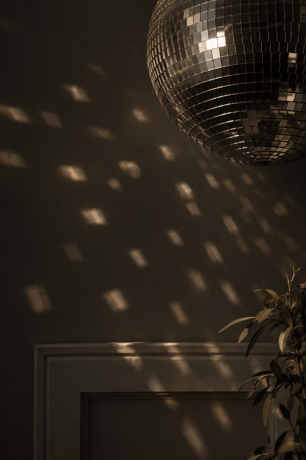 A disco ball hanging from the ceiling reflecting light, creating diamond-shaped light spots on the wall, with a potted plant to the right.