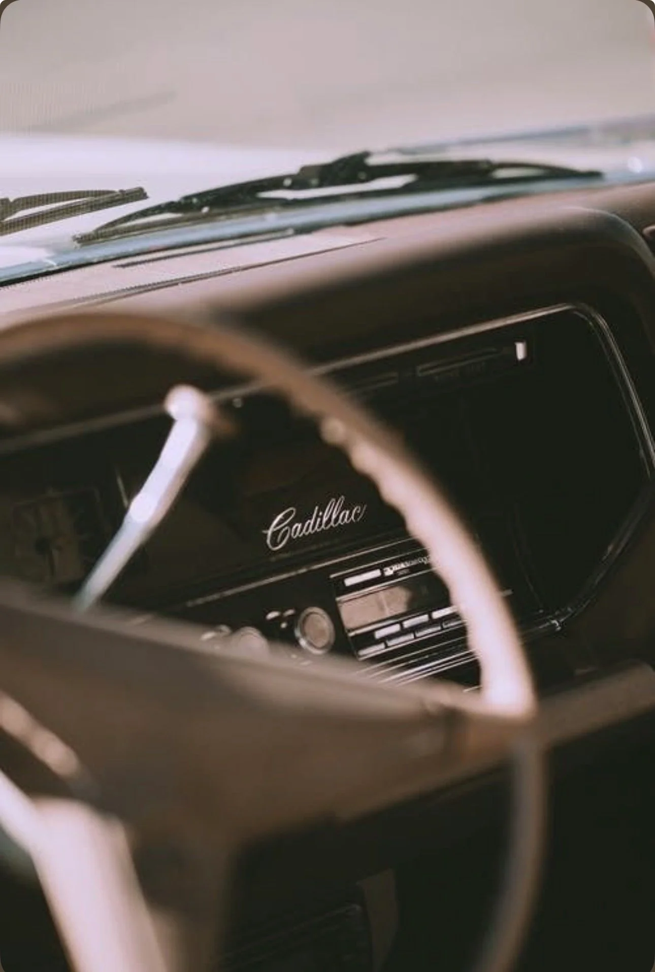 Inside a vintage Cadillac car, showing the dashboard and steering wheel with the Cadillac logo visible.