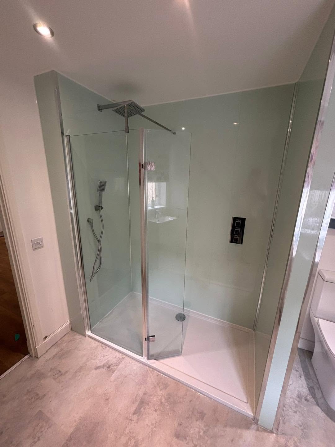 Glass shower enclosure with a rainfall showerhead and a handheld showerhead in a modern bathroom.