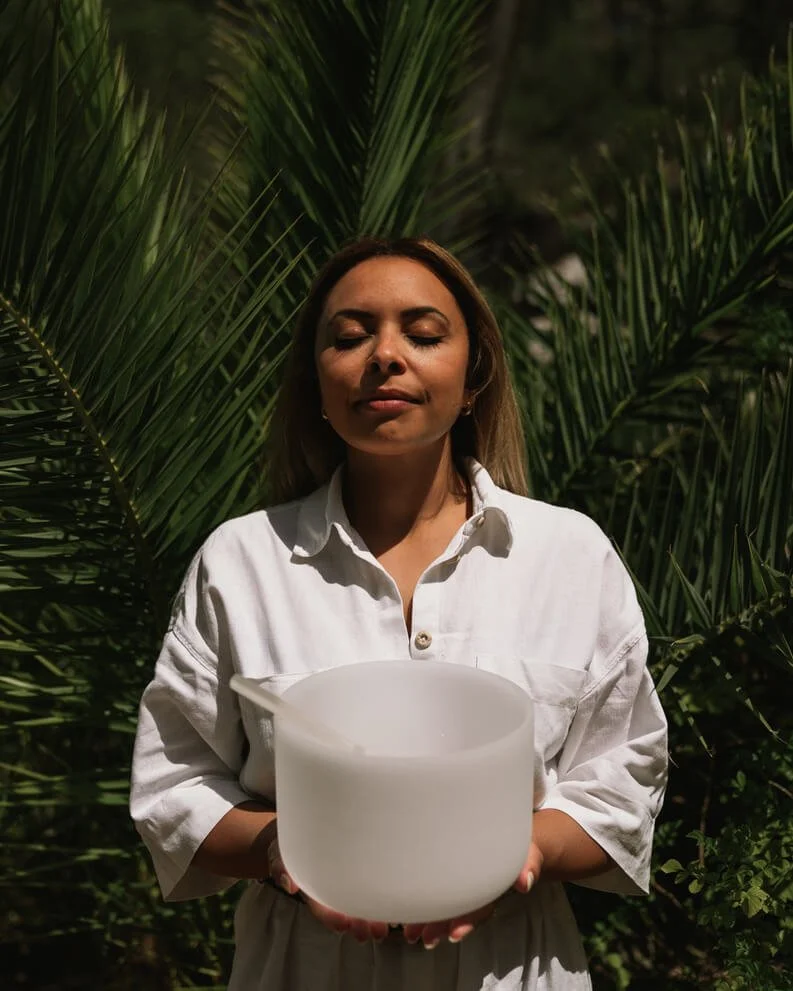 Becca Gayle-Phipps, founder of The Rest Room, holding a crystal singing bowl among palms in Mallorca