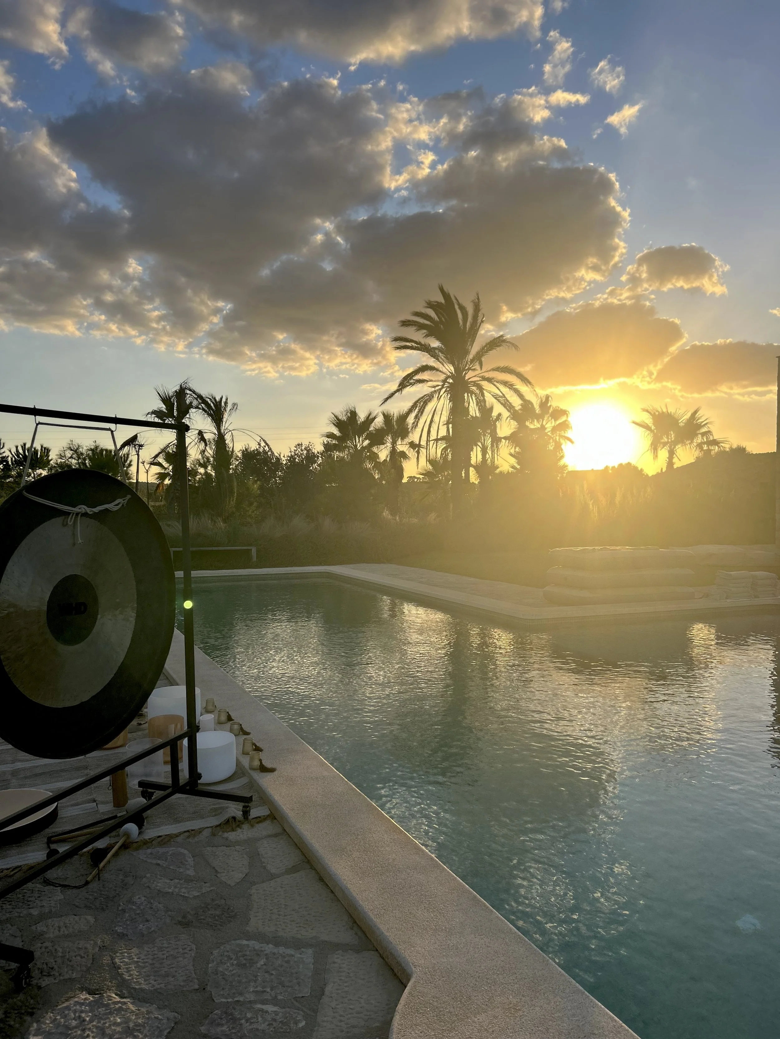 Gong and crystal bowls set beside a villa pool at sunset among palms in Mallorca, ready for a floating sound bath