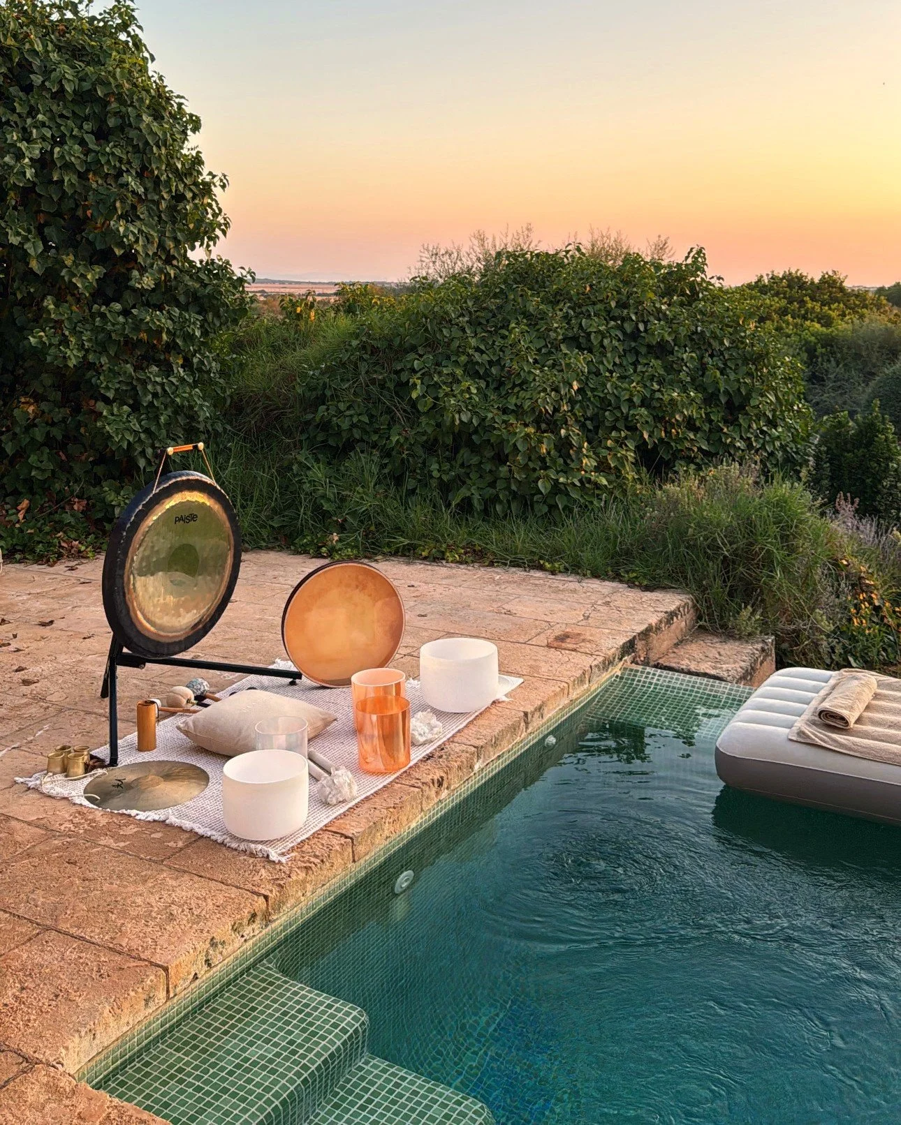 Crystal singing bowls, a gong and a floating bed set up beside a villa pool at sunset in Mallorca, ready for a private floating sound bath