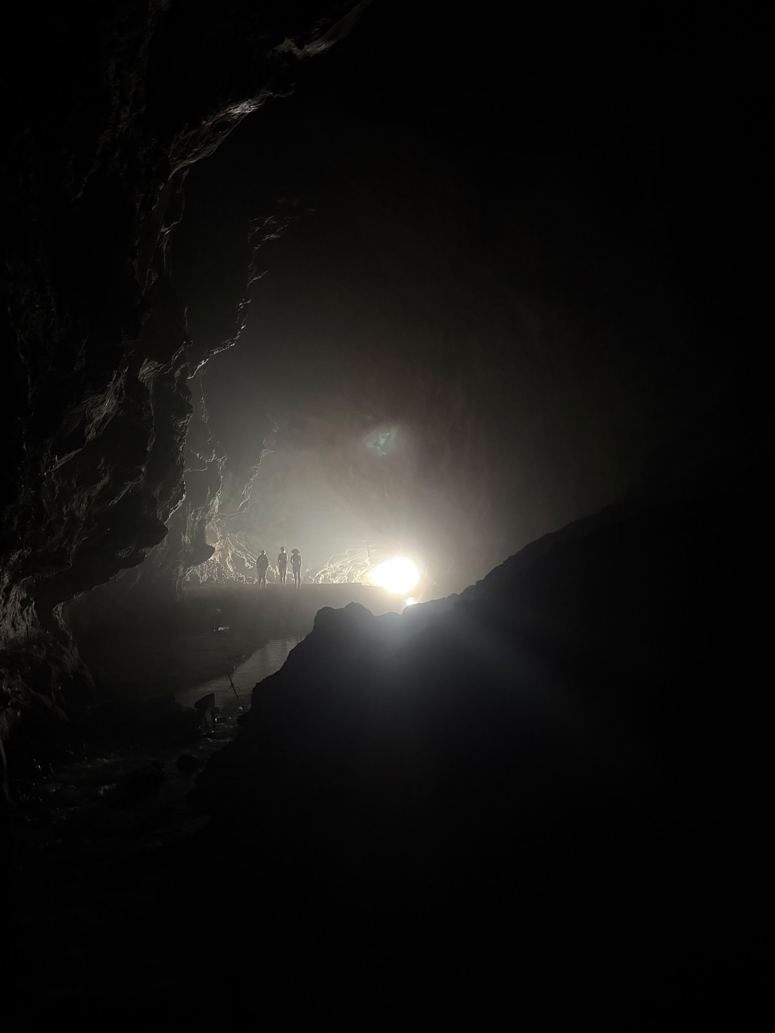 Silhouettes of three people walking inside a dark cave, with light shining from the entrance behind them.
