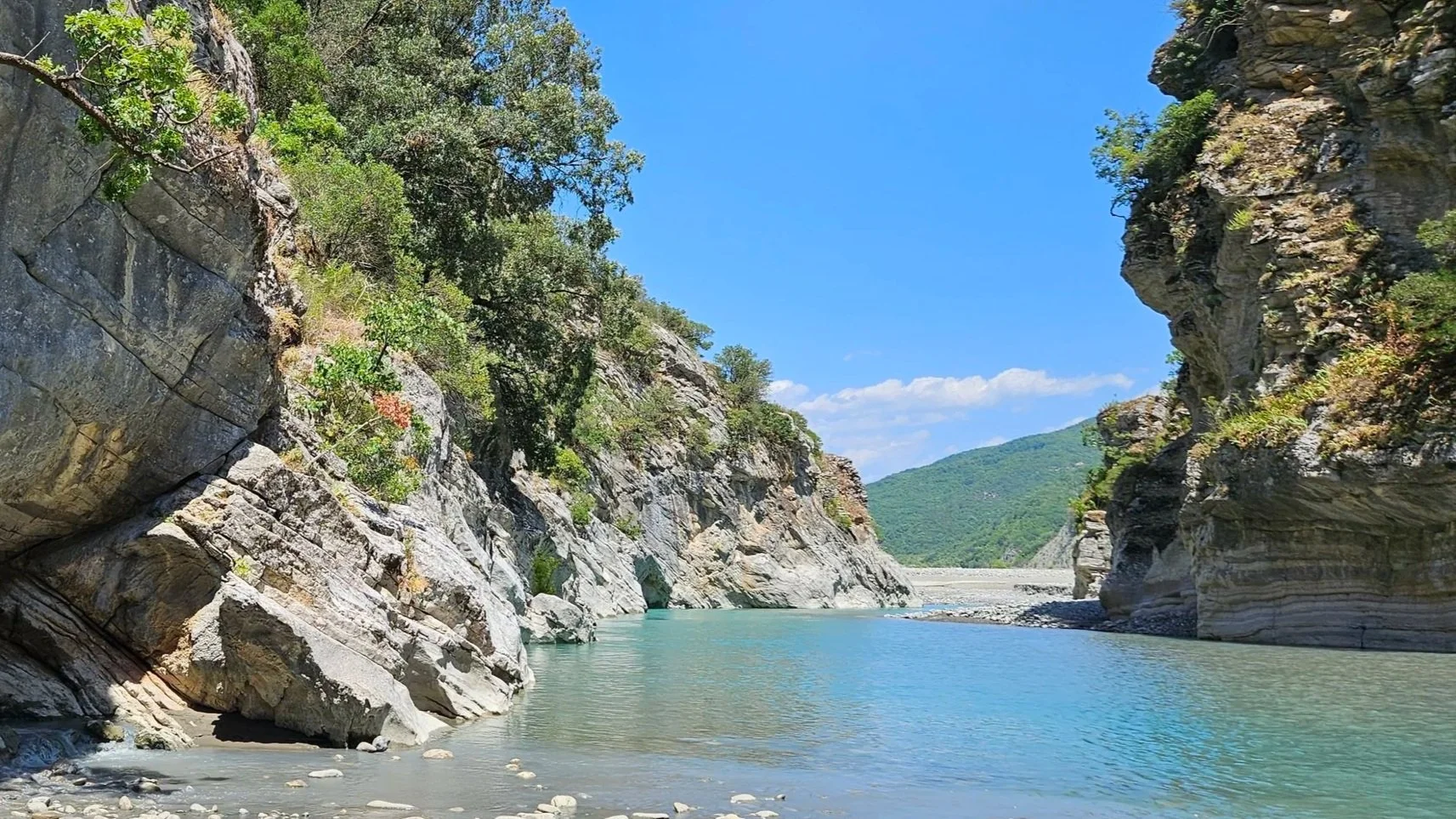 A river flowing through a canyon with steep, rocky walls covered in greenery under a clear blue sky.