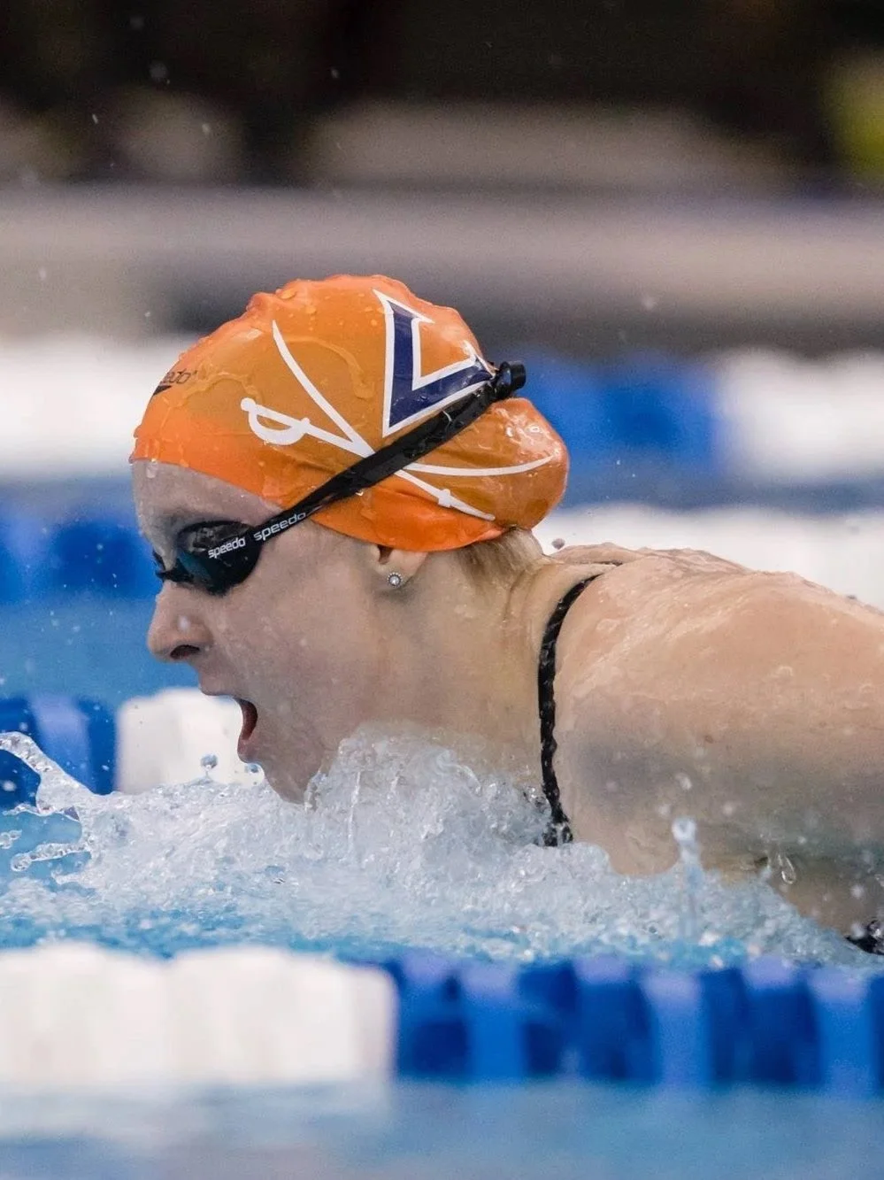 Close-up of a female swimmer with an orange swim cap and goggles, breathing out during a race in a swimming pool.